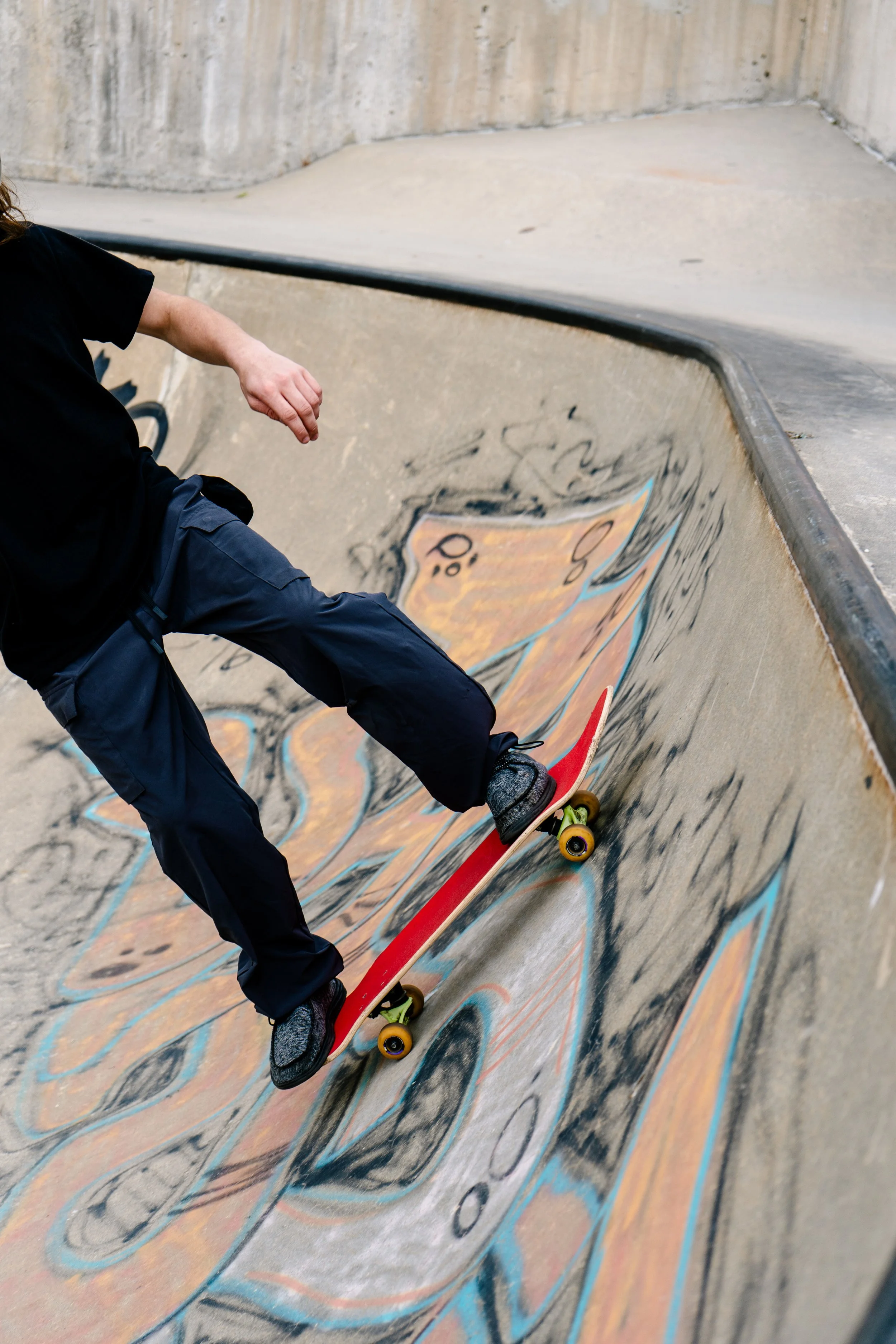 A person riding a skateboard in a concrete skatepark with graffiti art.