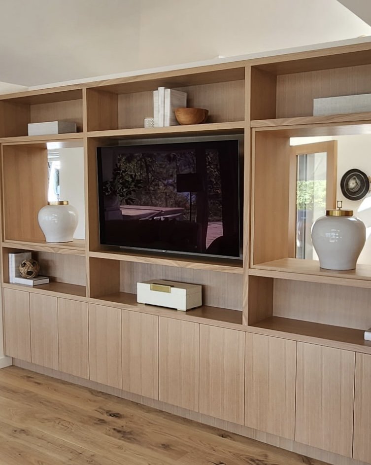 Wooden built-in entertainment center with open shelves, decorative vases, books, and a flat-screen TV in a living room.