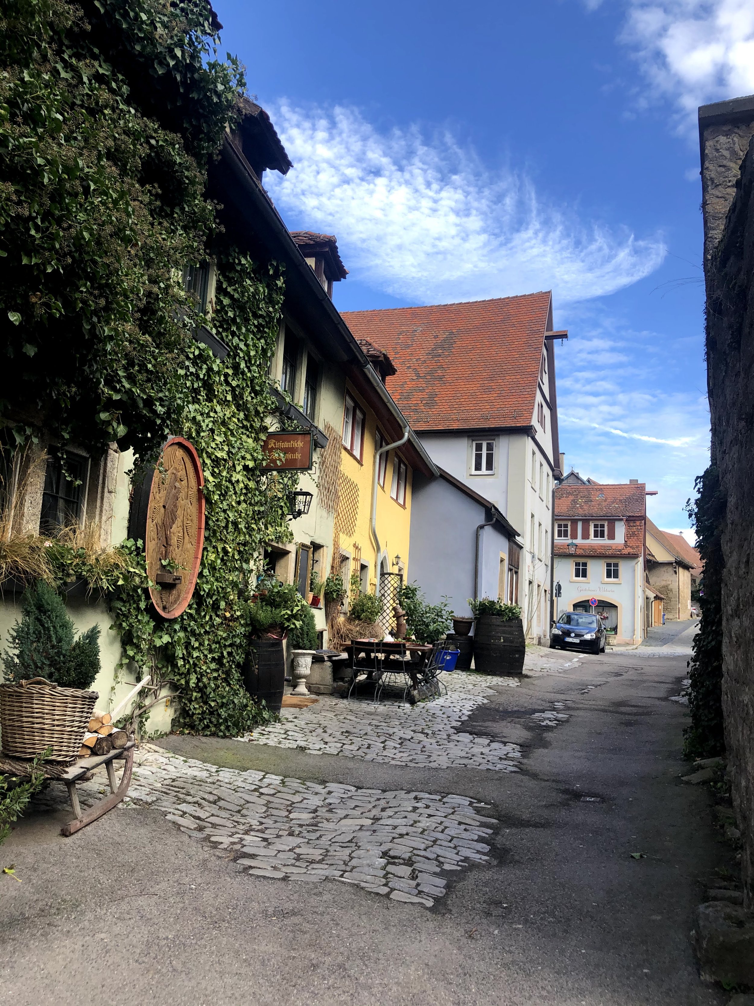 A narrow cobblestone street in Germany flanked by colorful European-style buildings, with a blue sky and some clouds above.