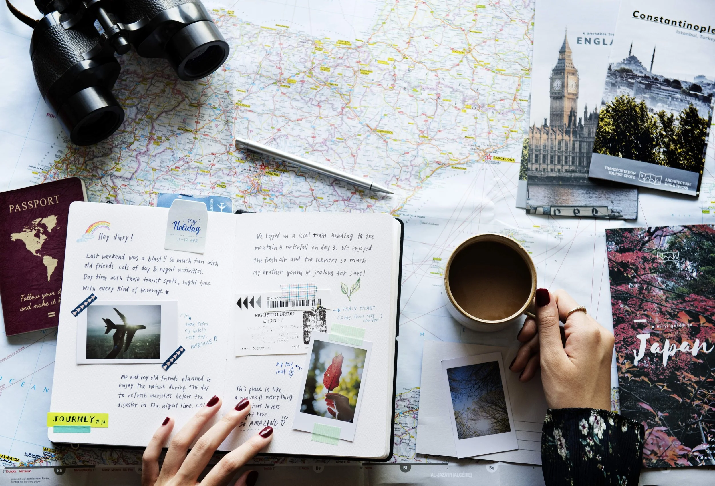 Travel planning scene with a map, postcards of Istanbul and Japan, a notebook with travel journal, a camera, a pen, a cup of coffee, a passport, and photographs.
