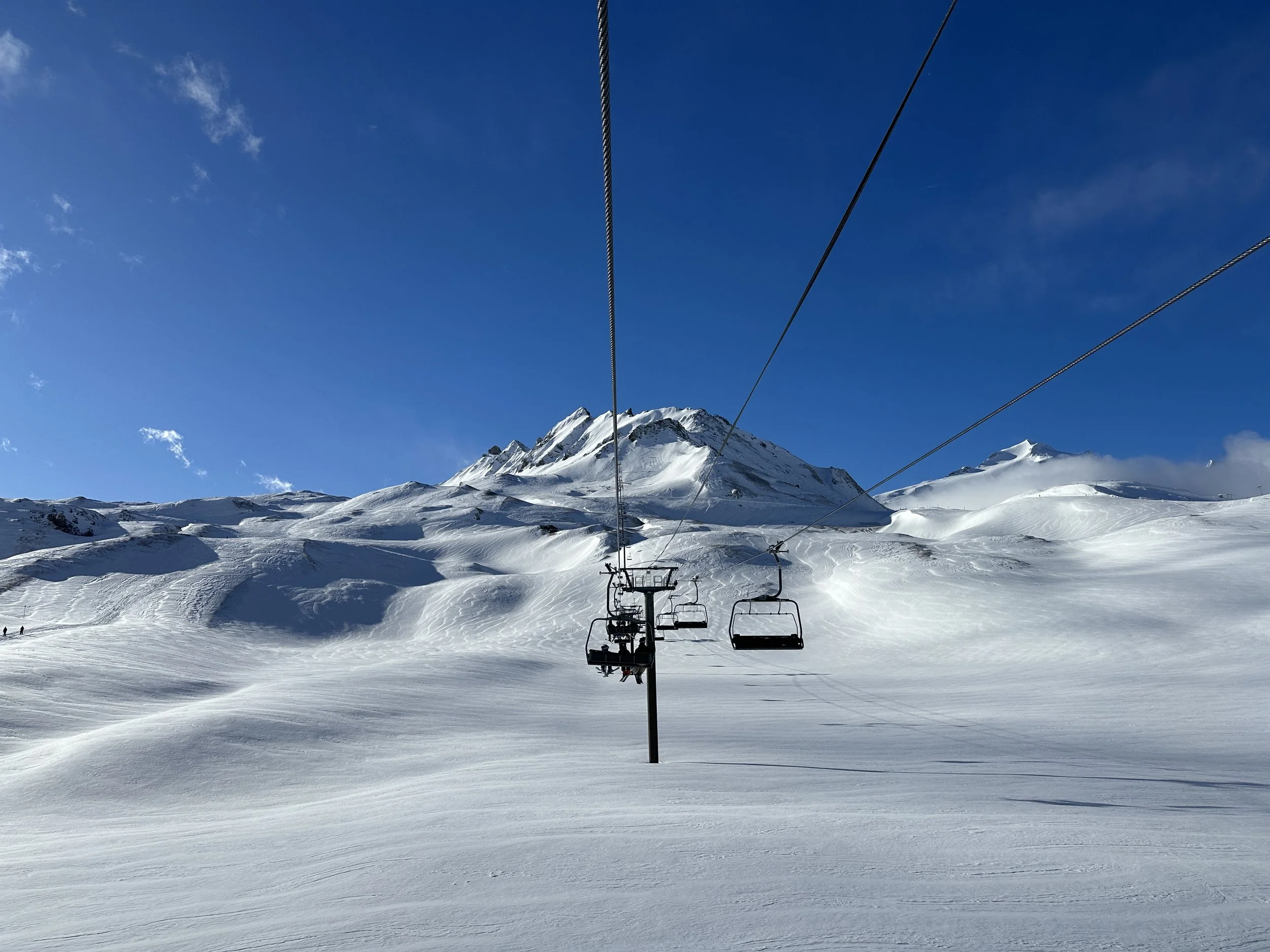 Snow-covered mountain in Val- D'sere, French Alps with ski lift chairs moving across the landscape under a blue sky with a few clouds.