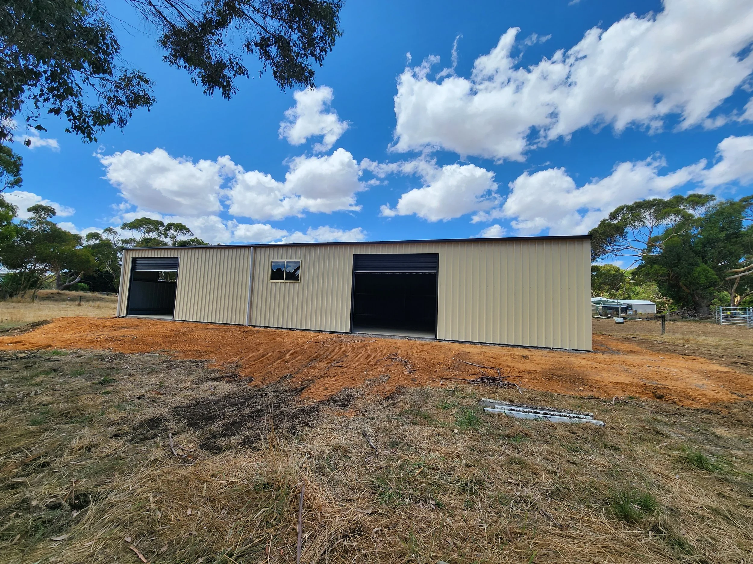 A beige metal shed with a small window and two open garage doors, built by M&C Sheds