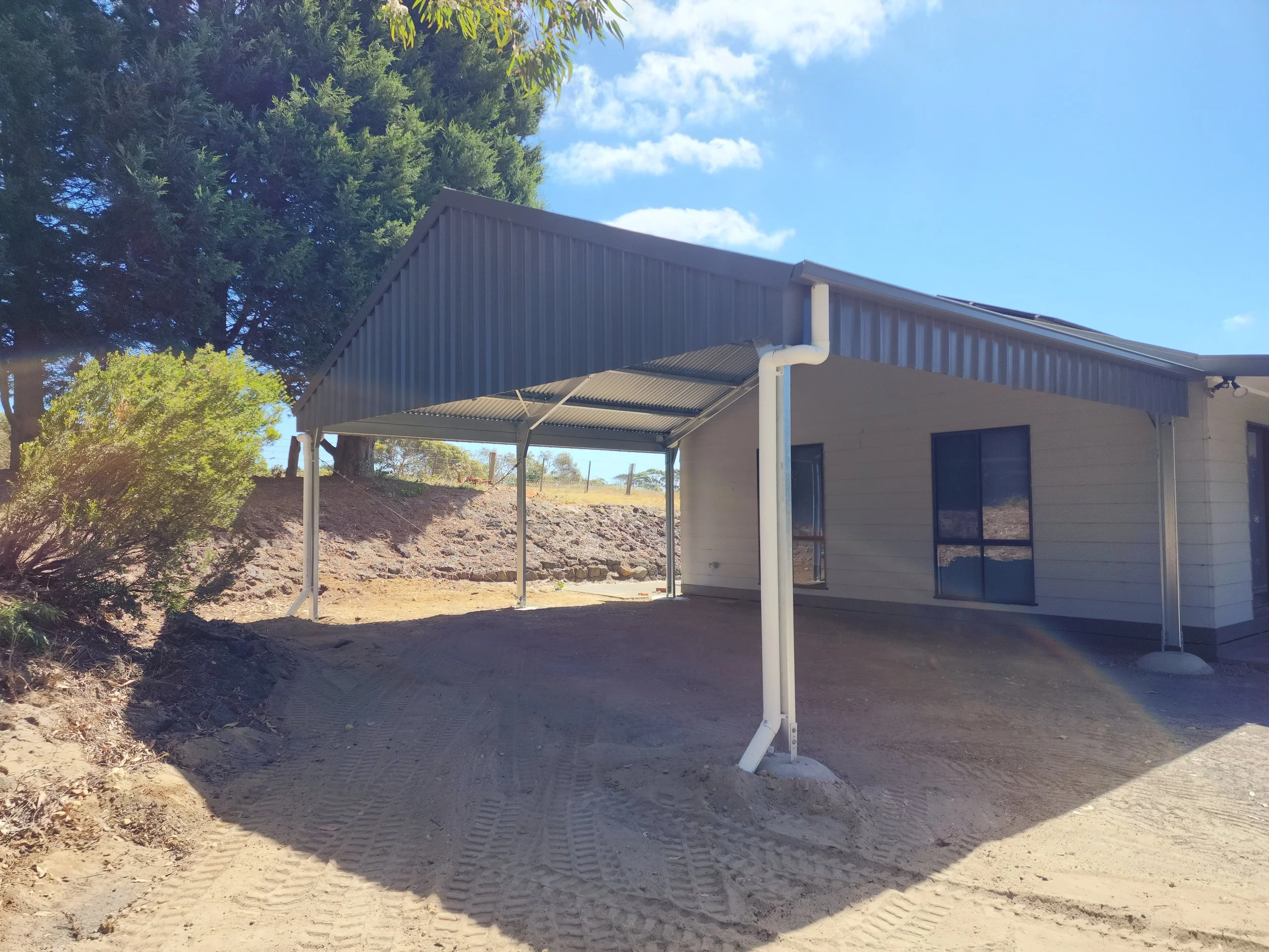 Newly constructed shed with a covered carport and a dirt driveway built by M&C Sheds