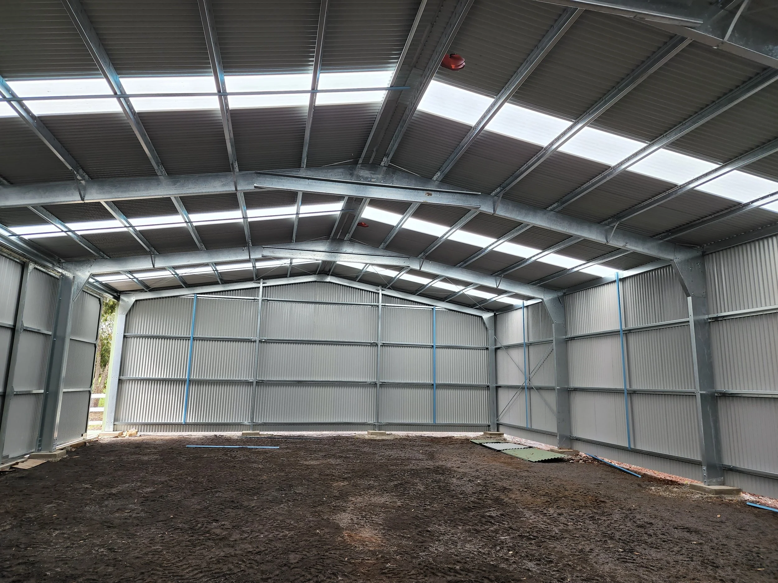 Interior of an unfinished metal building with metal walls and roof, dirt floor, and some construction materials on the ground.