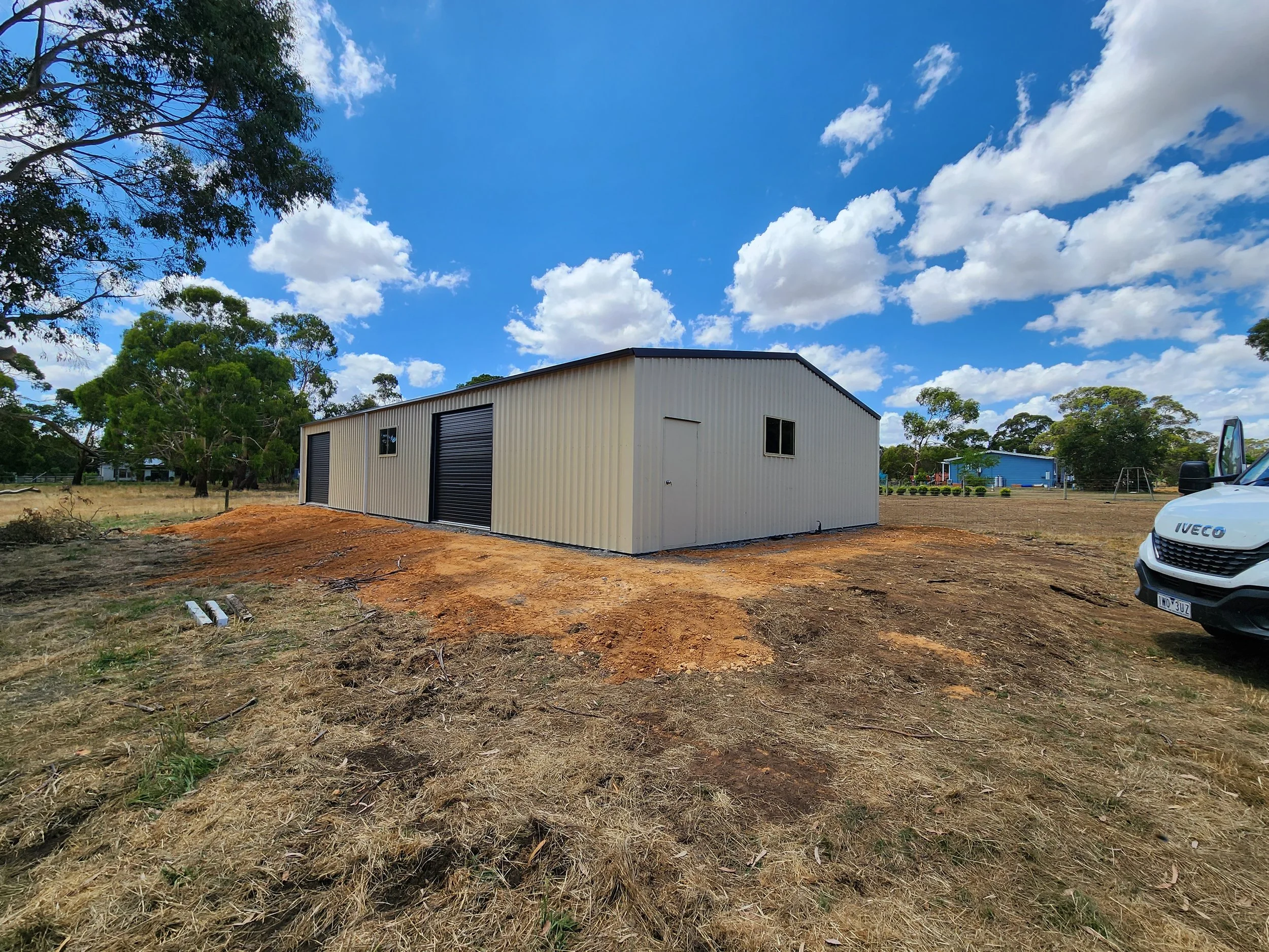 A metal storage shed with a black roll-up door, built by M&C Sheds