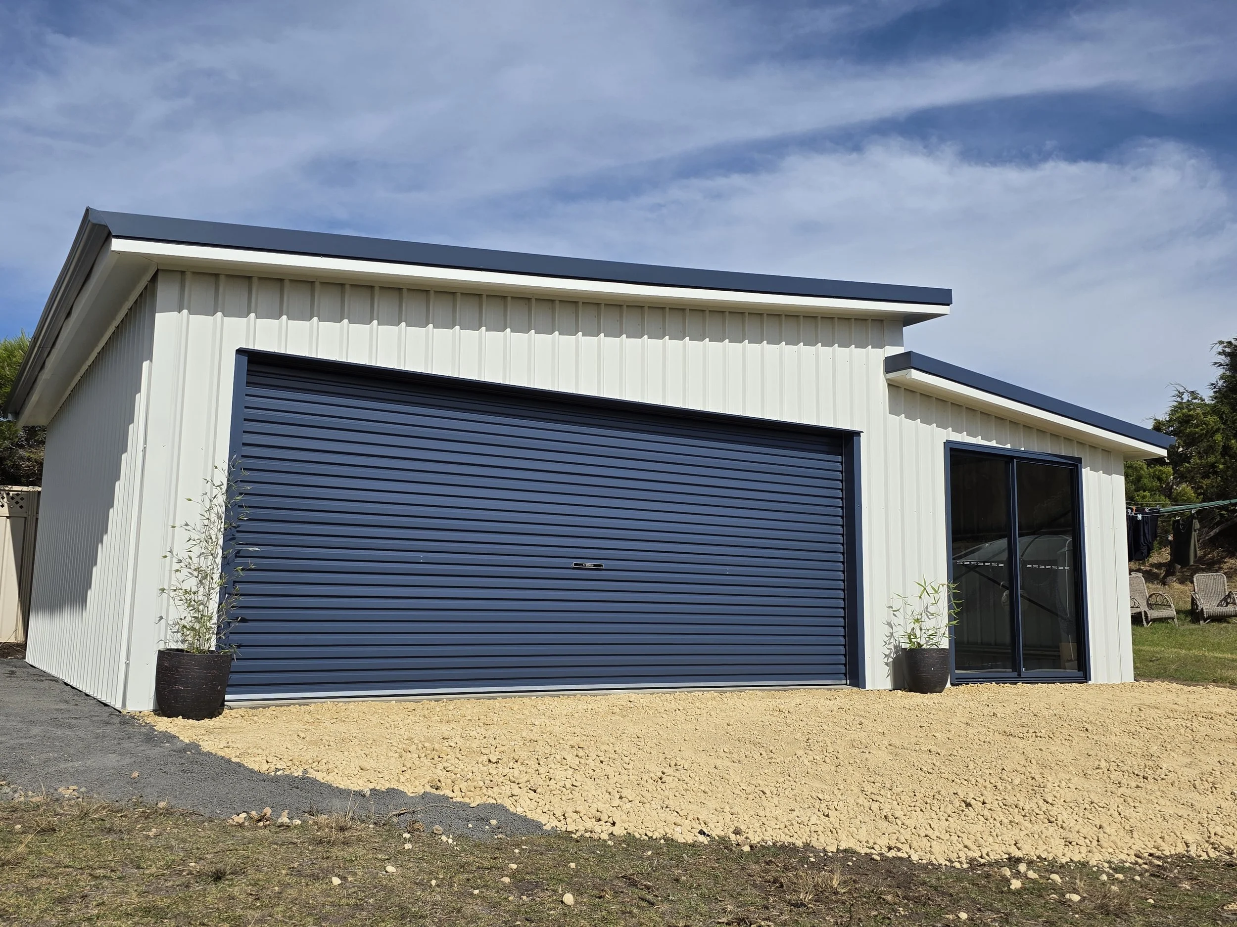 Modern garage shed with white exterior, blue rolling door, and large glass sliding door built by M&C Sheds