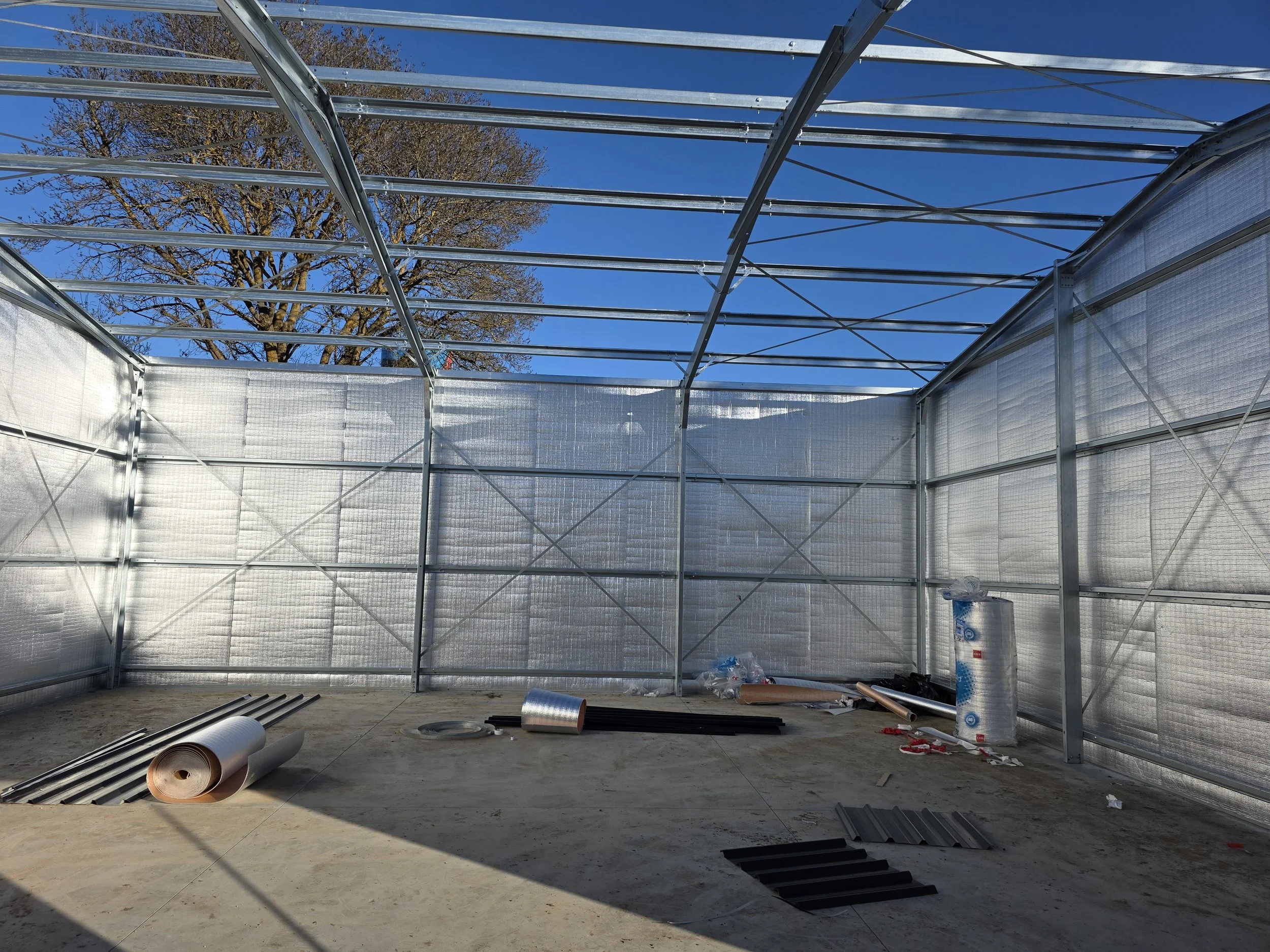 Interior view of a shed under construction with metal framing, insulation panels, and construction materials
