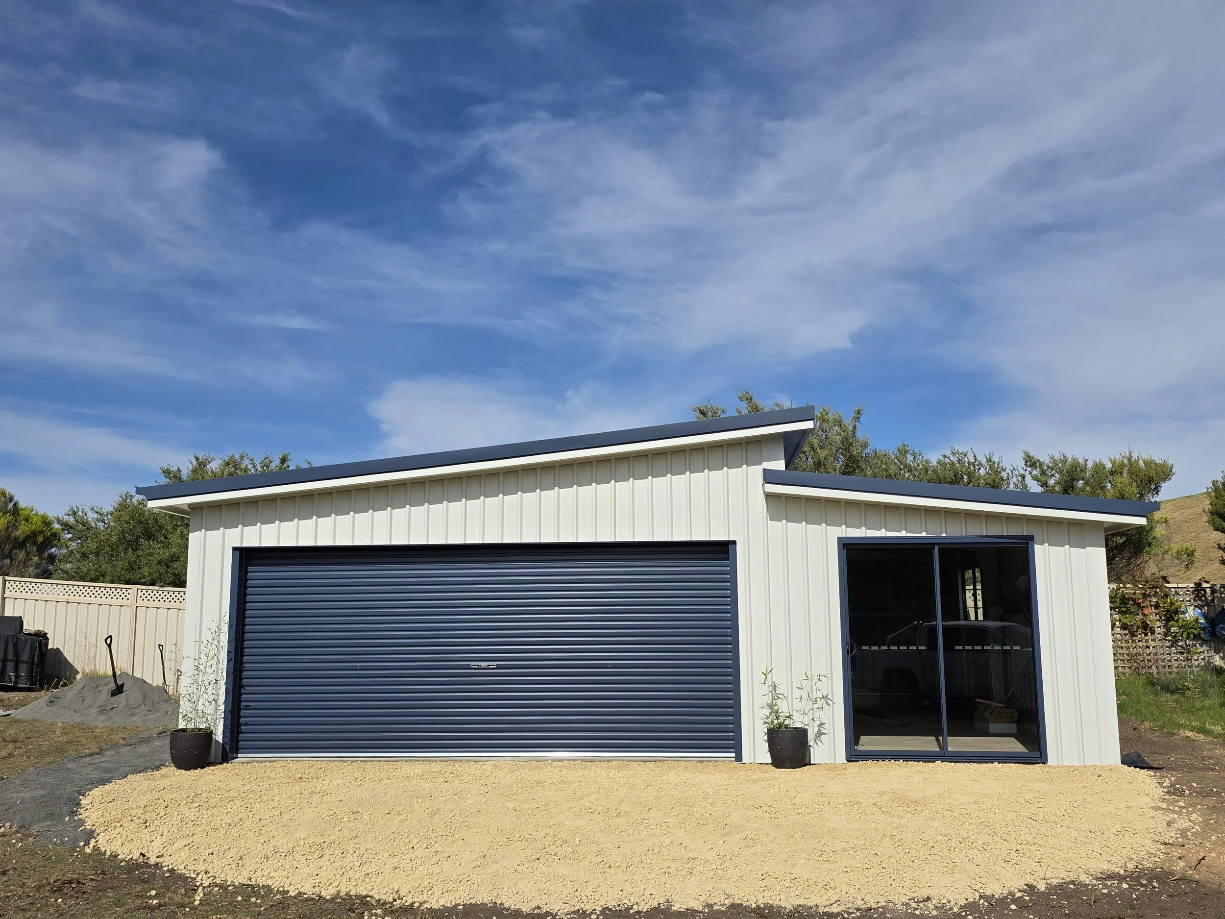 A modern small garage storage shed with metal siding and a blue roll-up door built by M&C Sheds