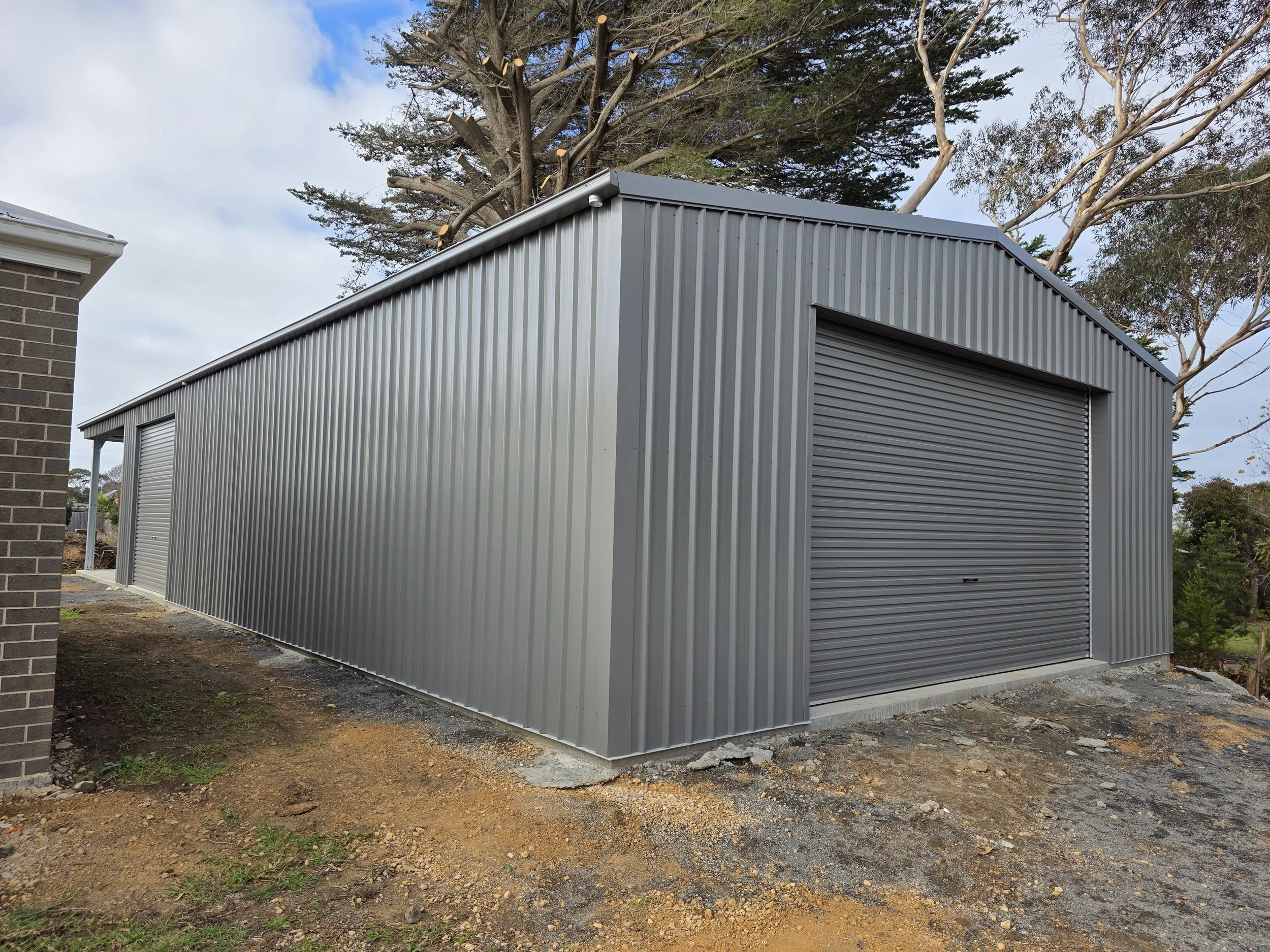 A gray metal storage shed with roll-up doors built by M&C Sheds