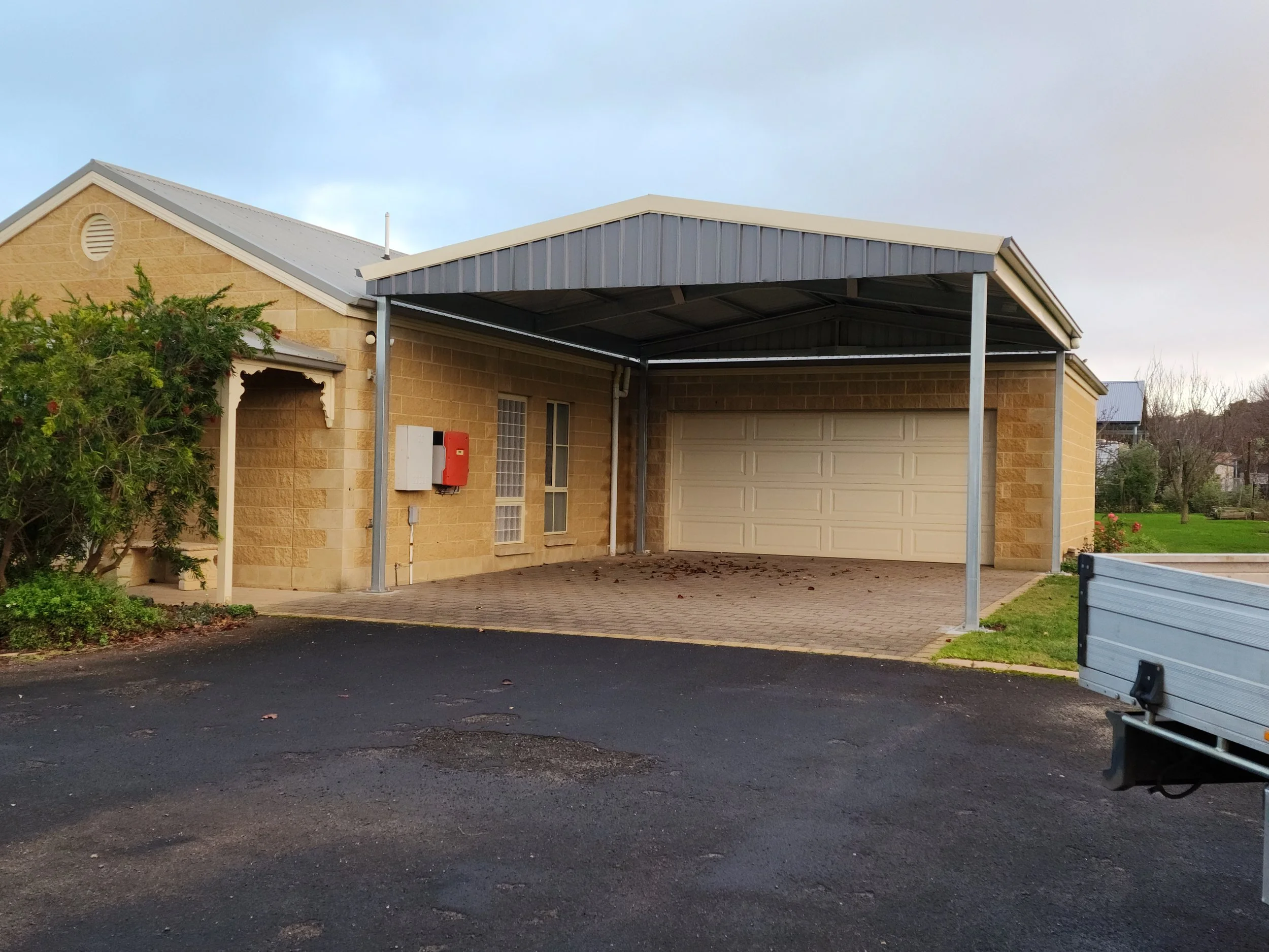 Front of a house shed with a covered carport, beige brick walls, a white garage door, built by M&C Sheds