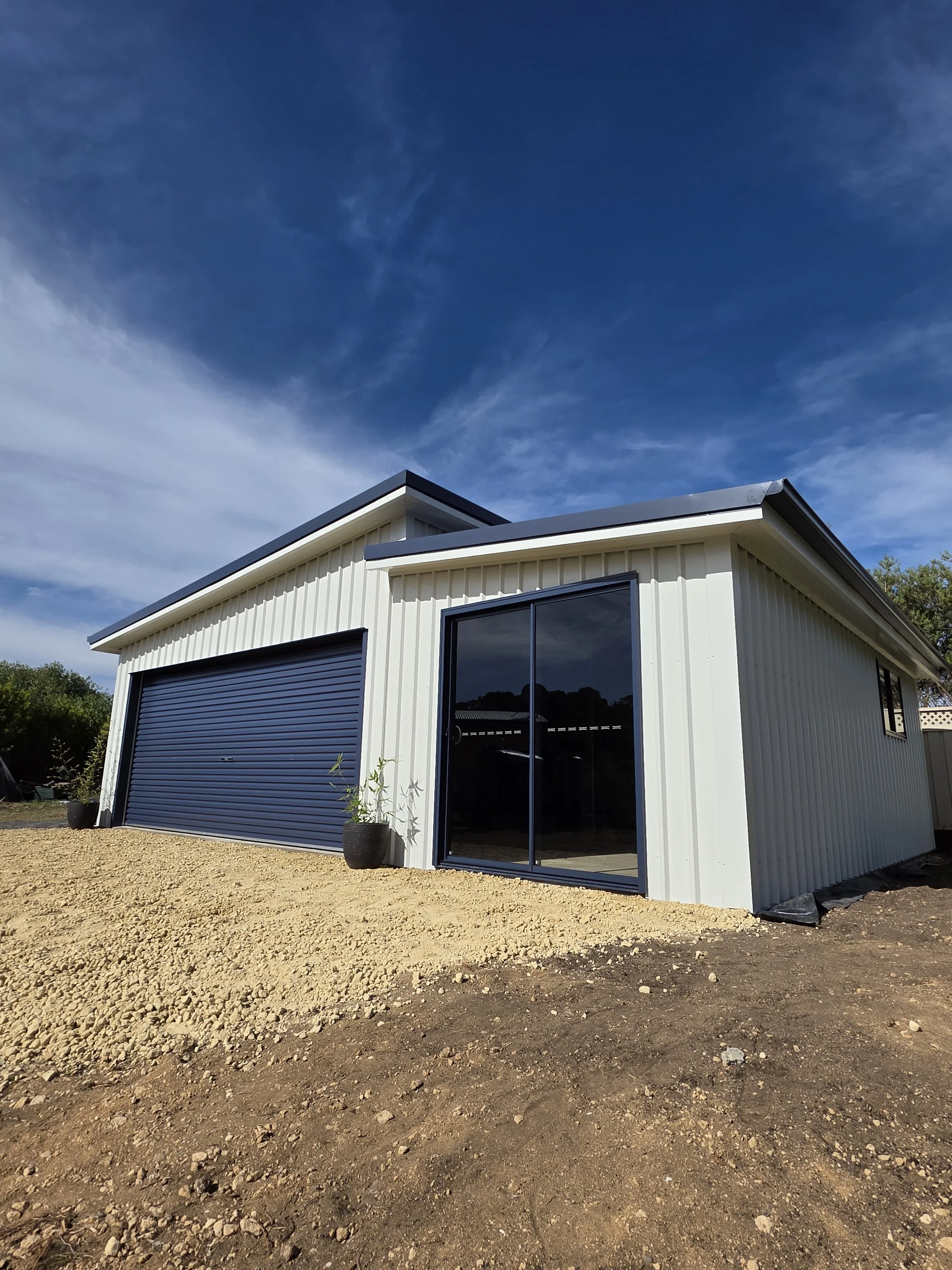A modern white building with a blue garage door and sliding glass doors under a blue sky.