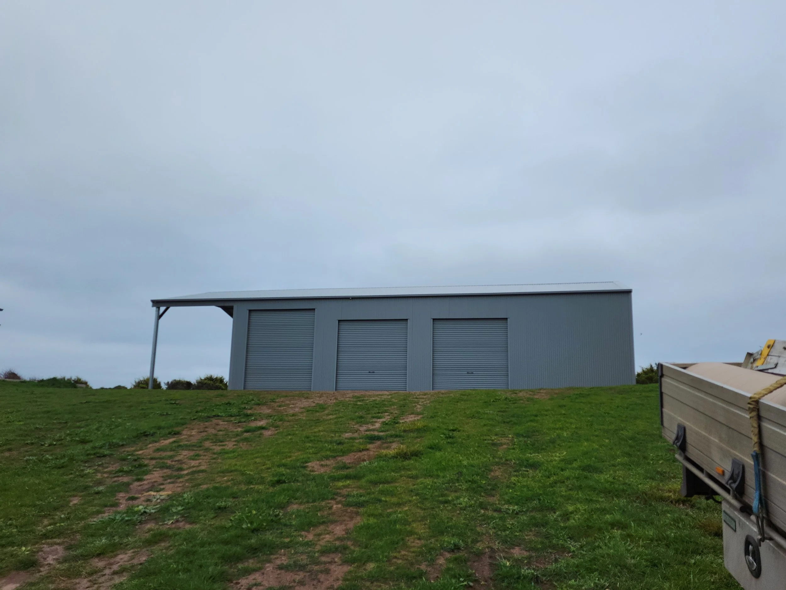 A gray metal storage building with three roll-up garage doors, built by M&C Sheds