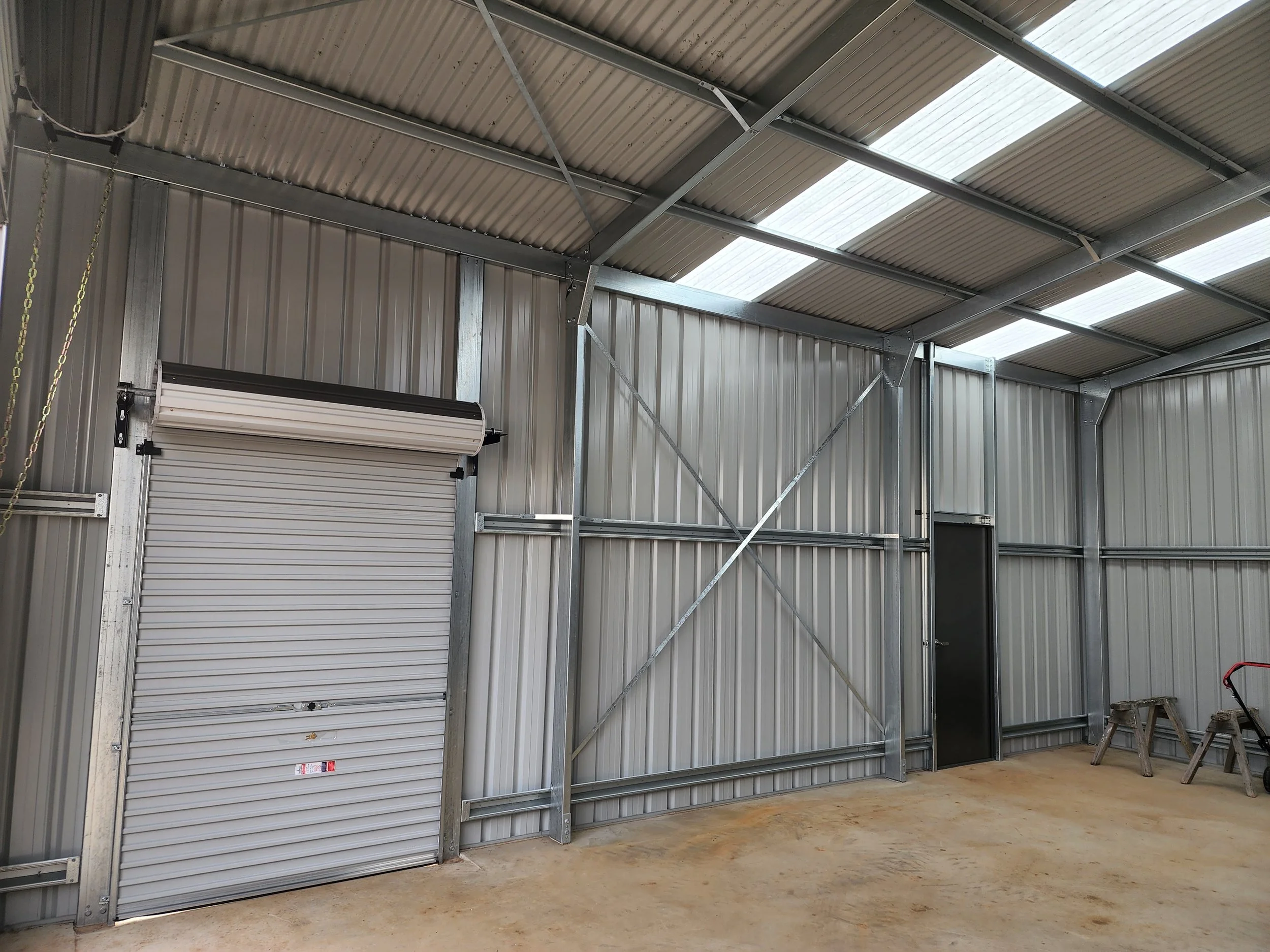 Interior of a new metal storage shed or garage with a closed roll-up door, a small black door, and a concrete floor.