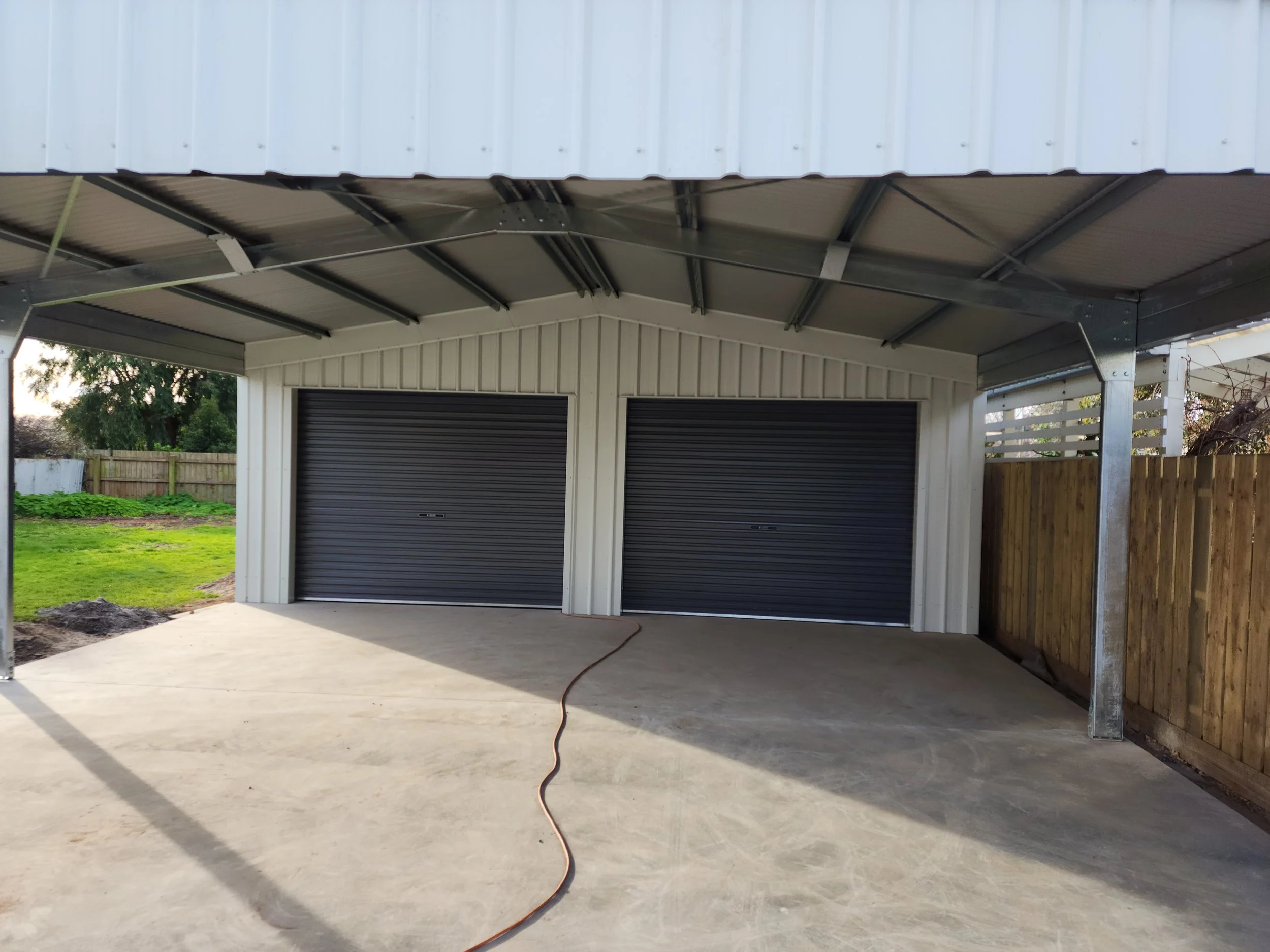 Outdoor garage shed with two closed black roll-up doors and a concrete floor, built by M&C Sheds