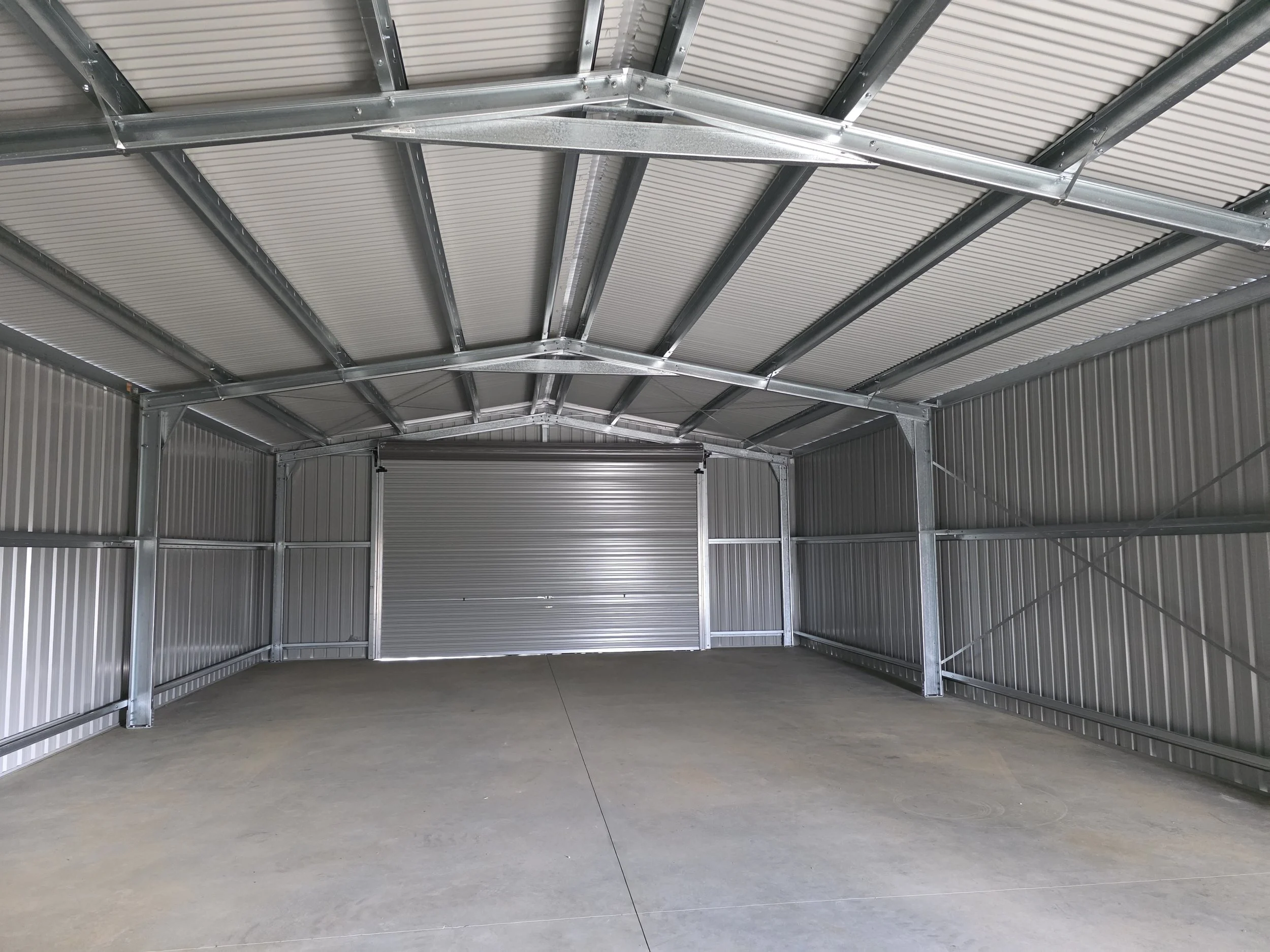 Metal storage shed unit with a concrete floor, metal walls, and a closed rolling door.