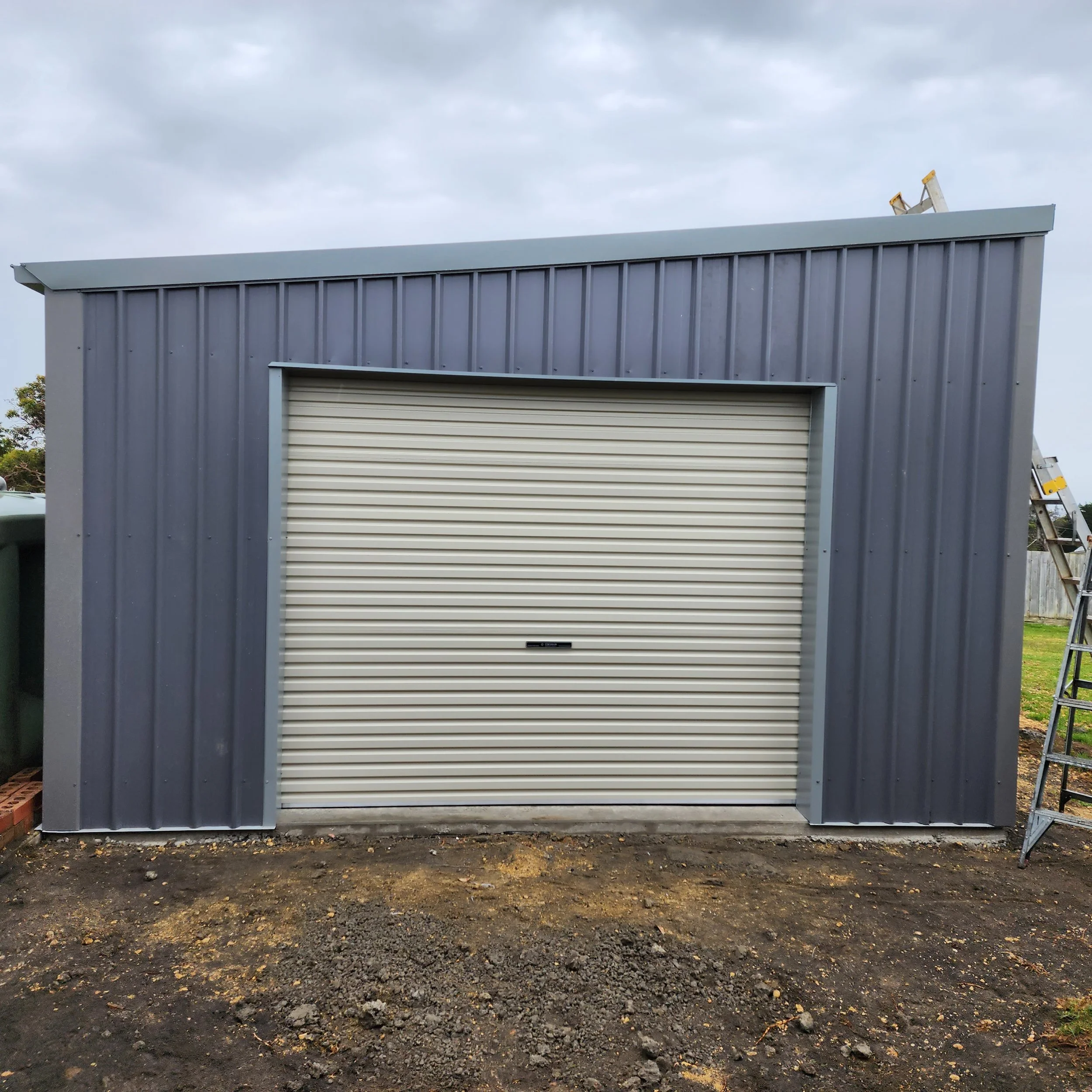 Gray metal shed with a closed roll-up door built by M&C Sheds