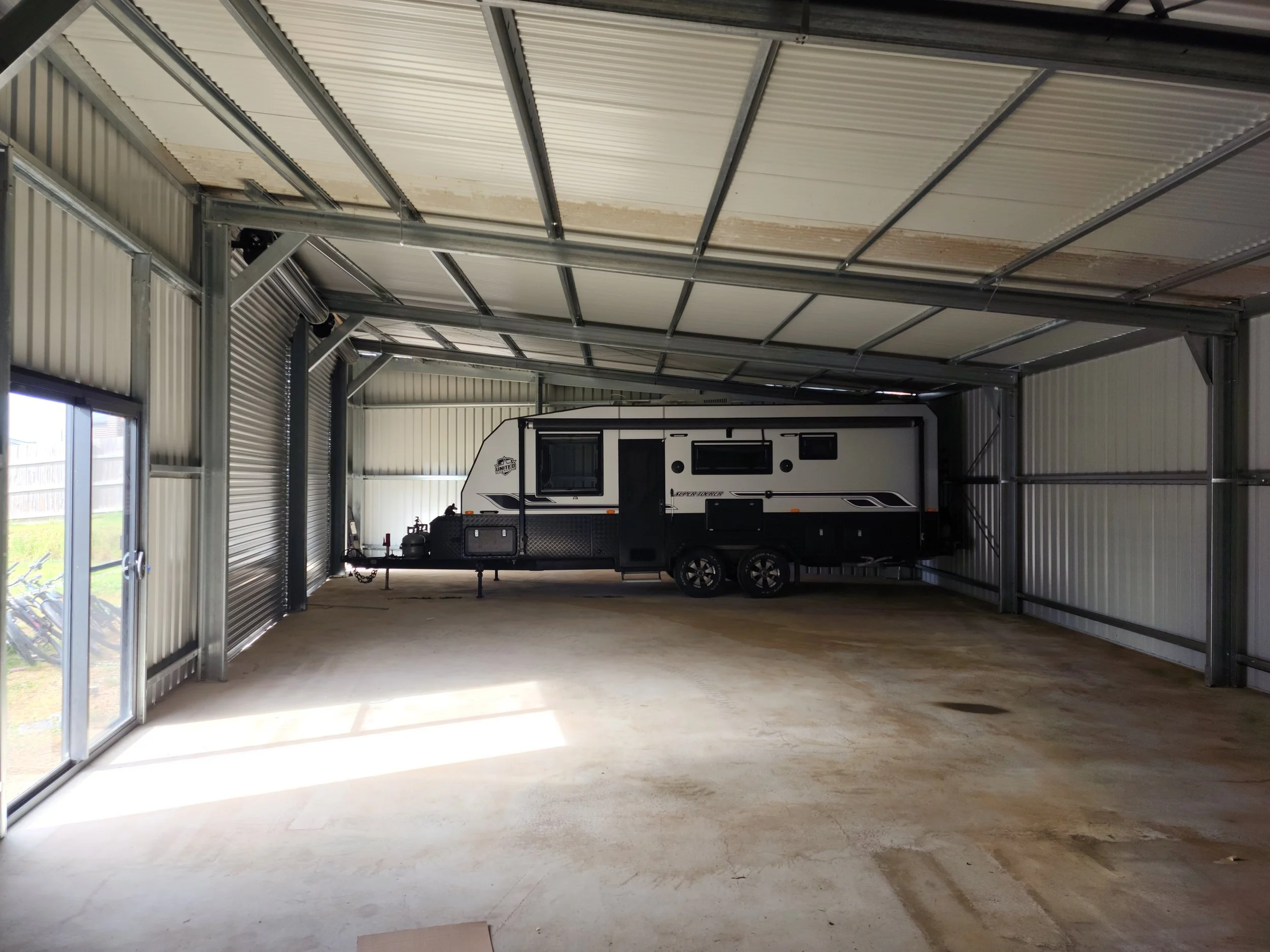 Interior of a metal storage building with a parked black and white travel trailer.