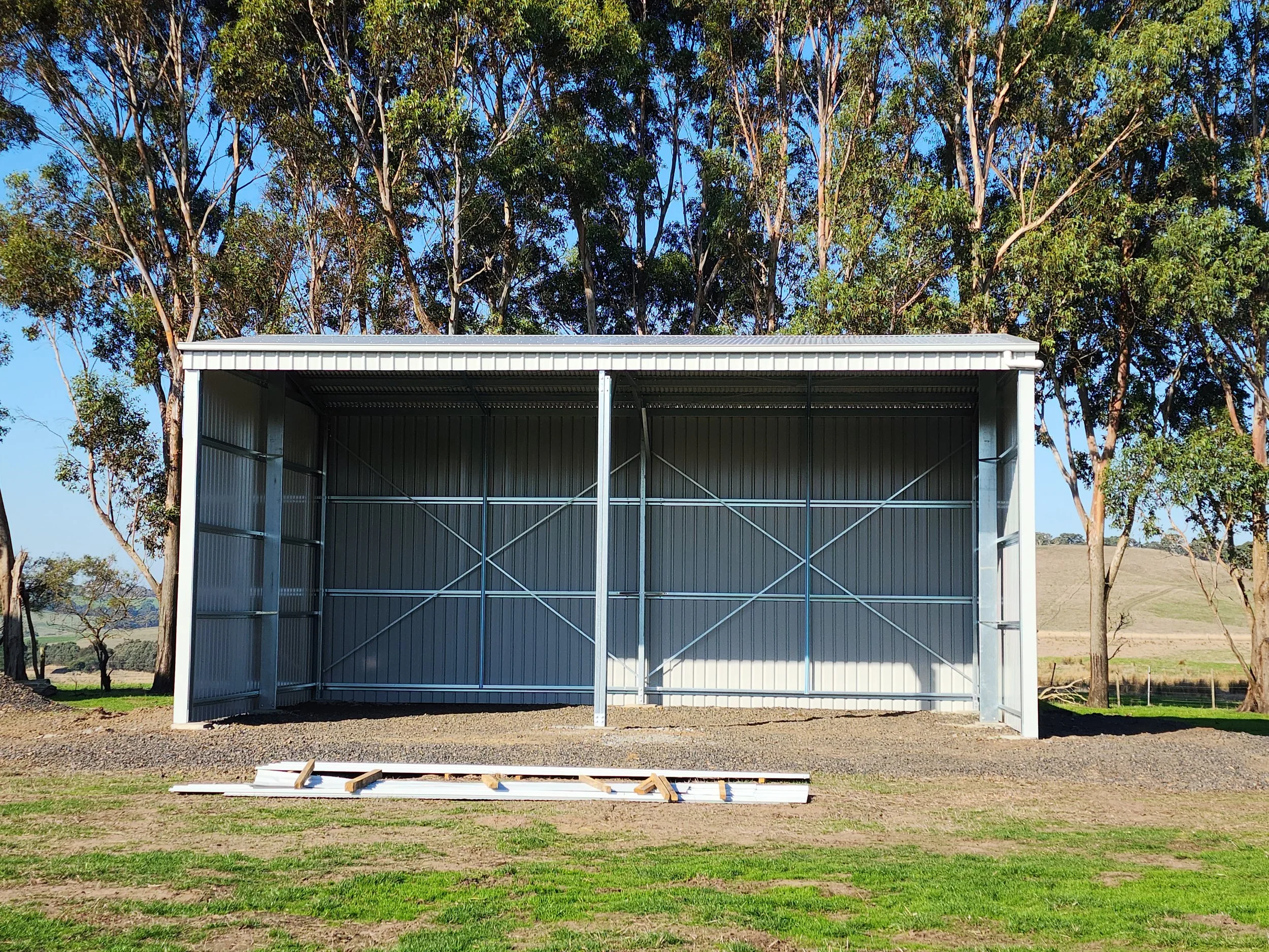 Empty metal storage shed on a grassy field with trees in the background.