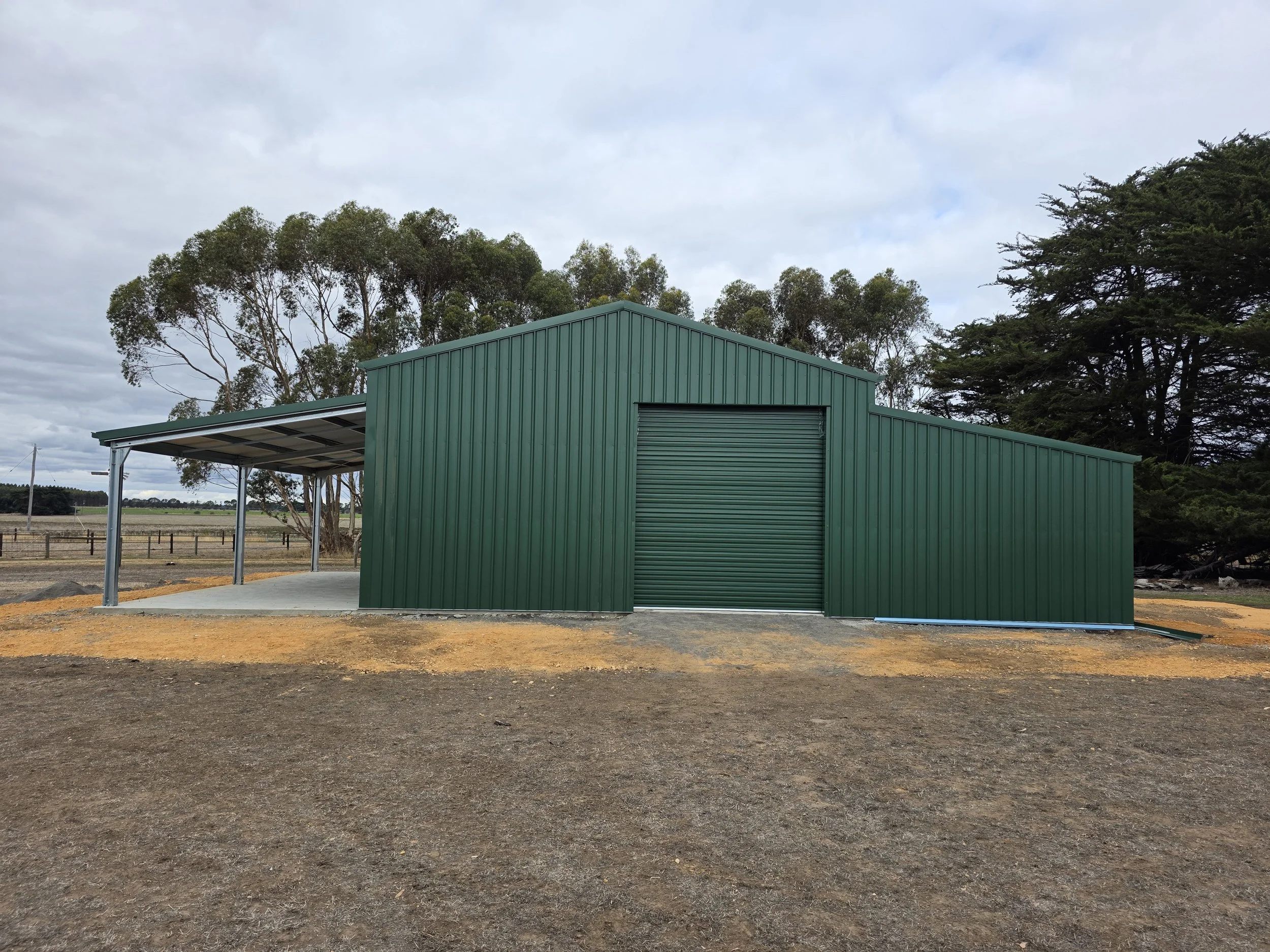 Green metal shed with roll-up door built by M&C Sheds