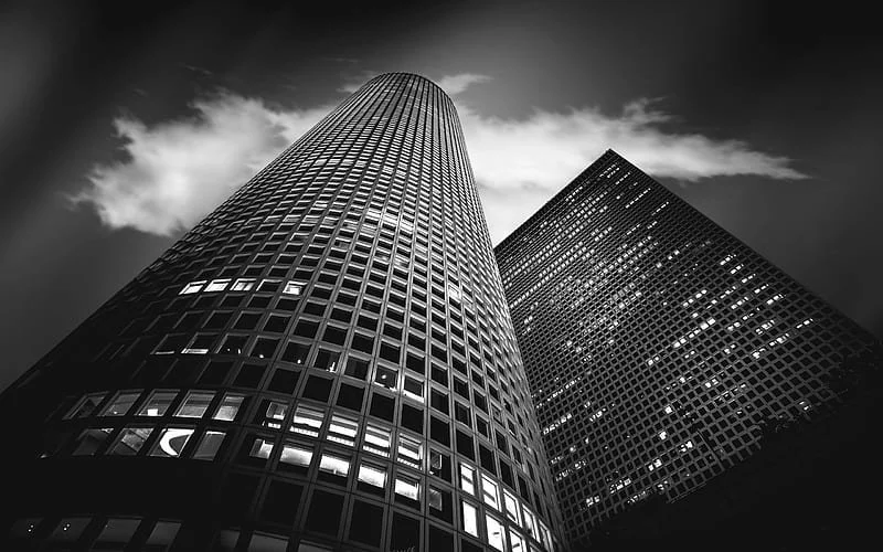 Black and white photo of two tall skyscrapers from a low angle, showing the grid-patterned windows and modern architecture.
