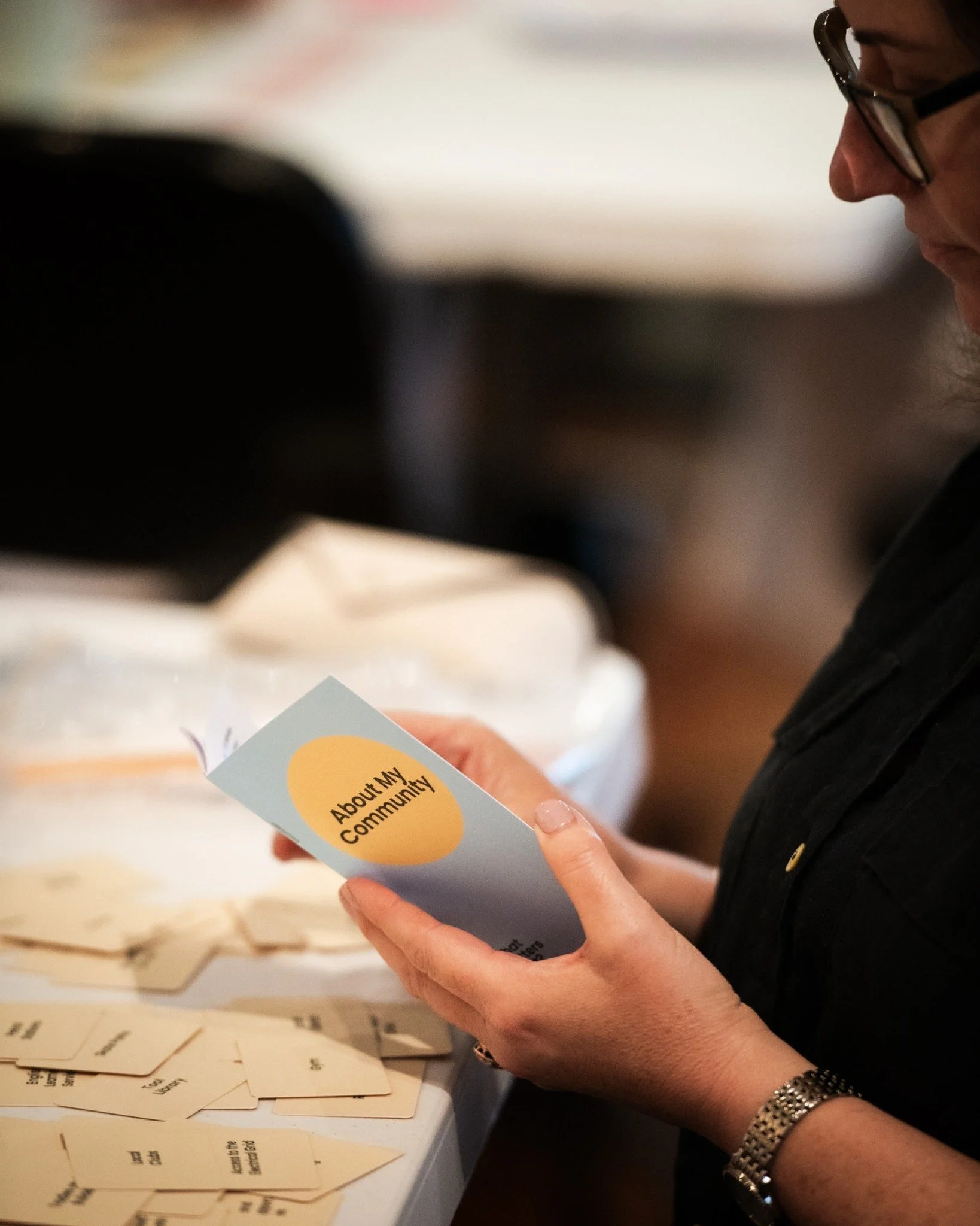 Person holding a pamphlet titled 'About My Community' at an event with scattered informational cards on a table.