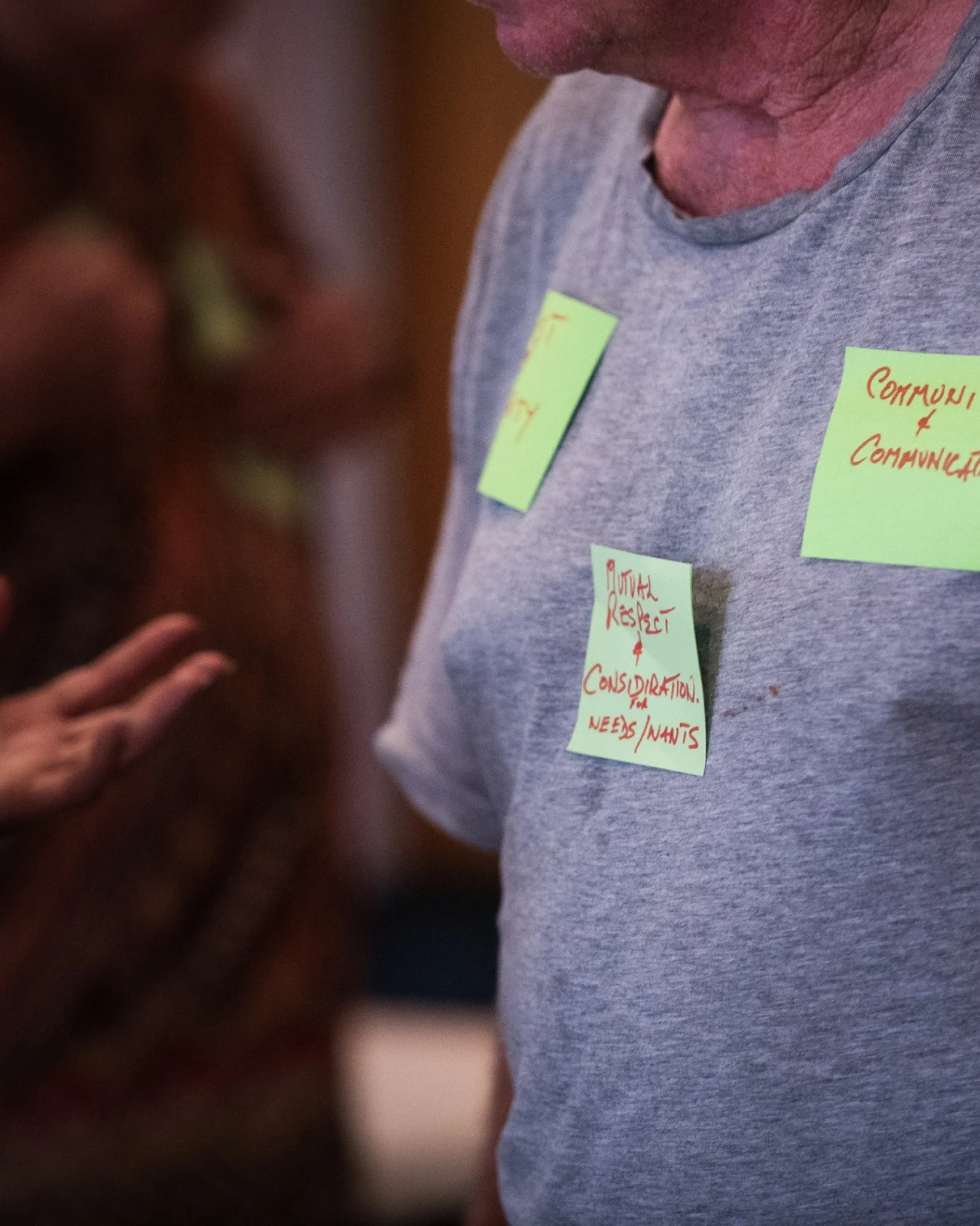 Close-up of a person wearing a gray shirt with green sticky notes attached, featuring handwritten red text about communication, mutual respect, and consultation.