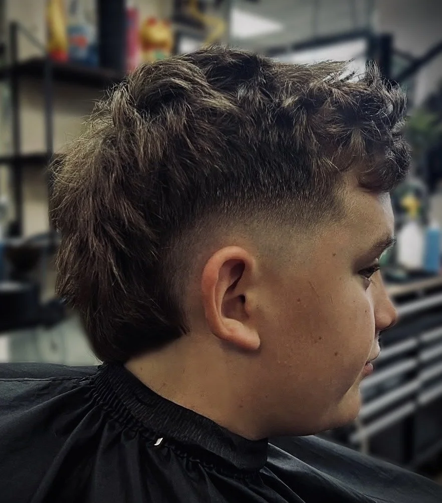 Young person with a textured, layered haircut featuring a fade on the sides at a barber shop.