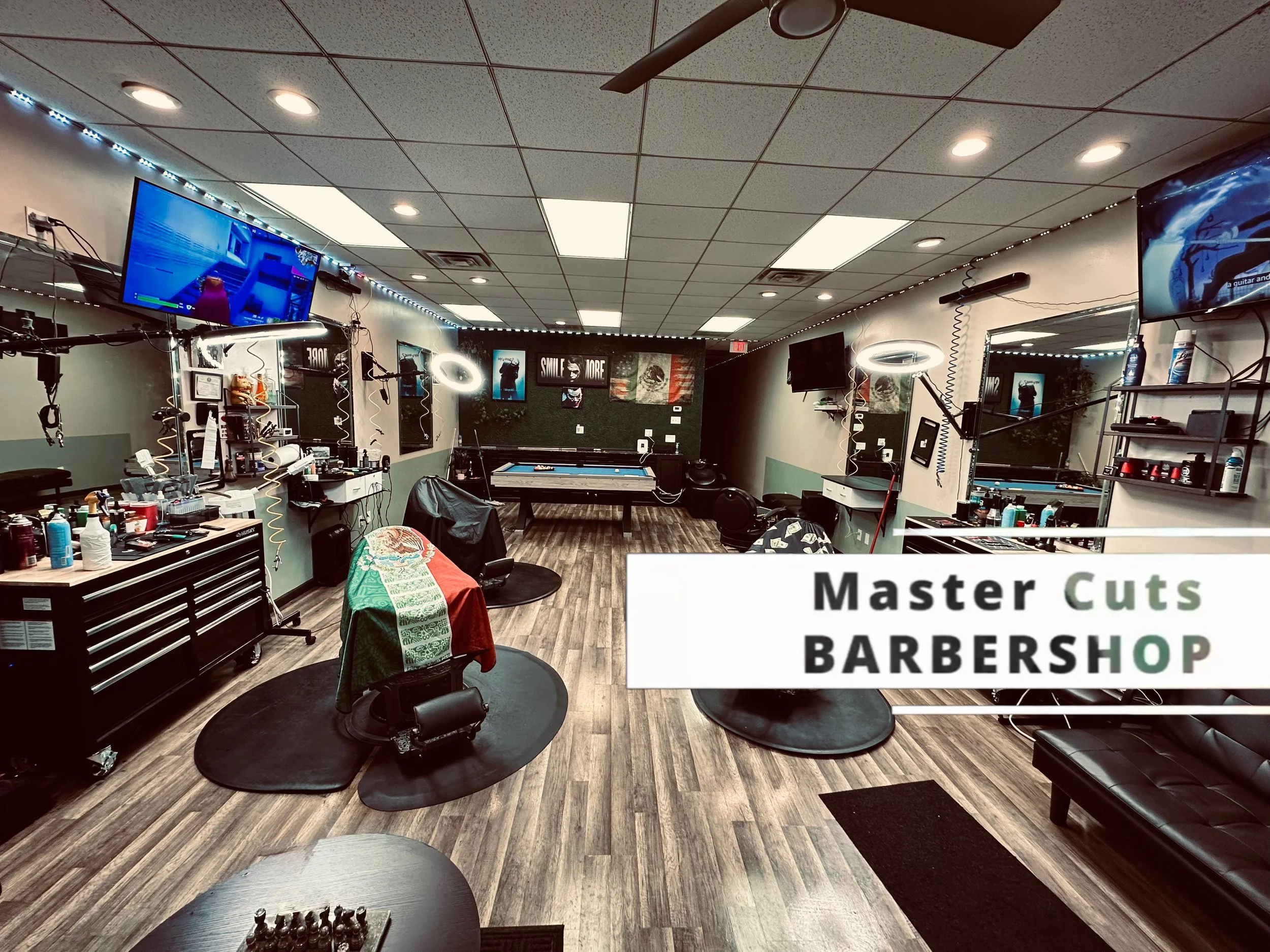 Interior of a barbershop with barber stations, mirrors, TVs, and a pool table at the back.