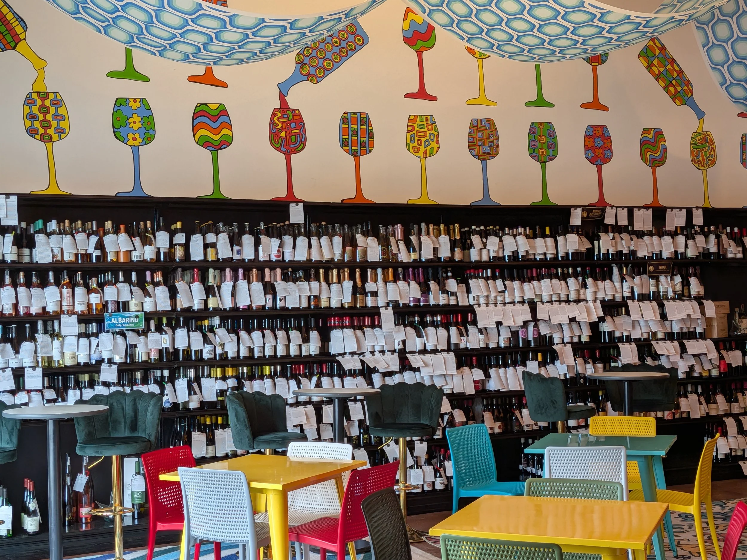 Shelves full of wine and a hand painted mural of wine glasses and bottles above at Dashi Wine Bar