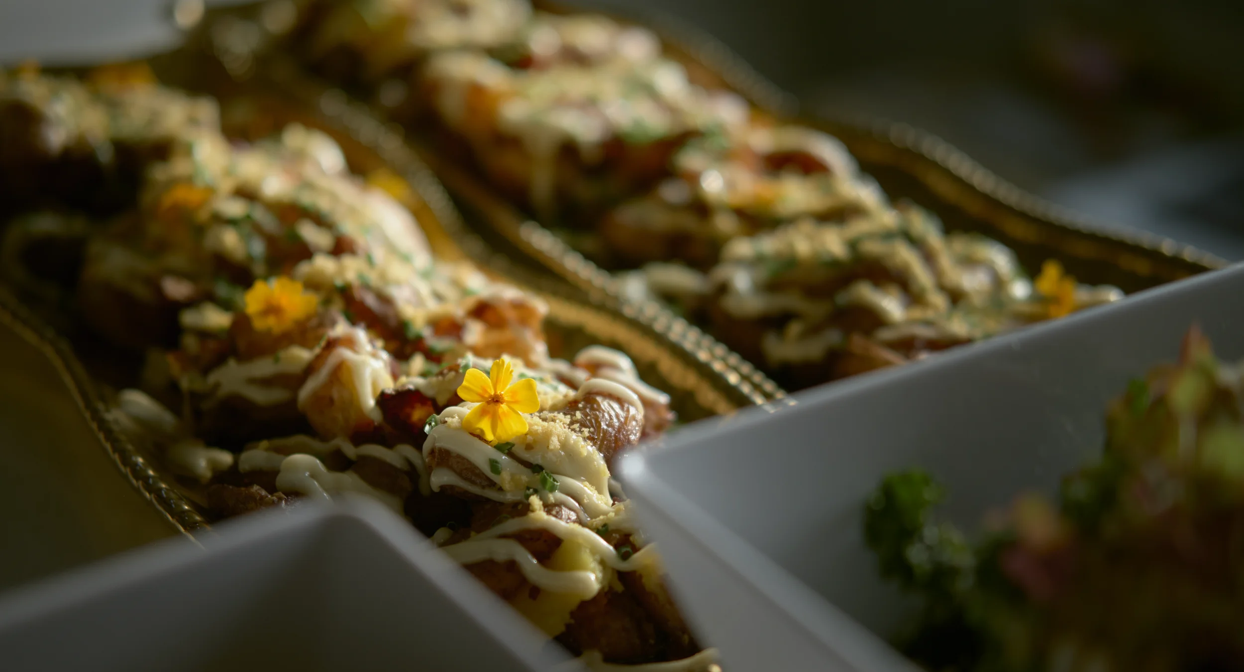 Close-up of topped nachos with melted cheese, sauce, and a yellow edible flower on a tray