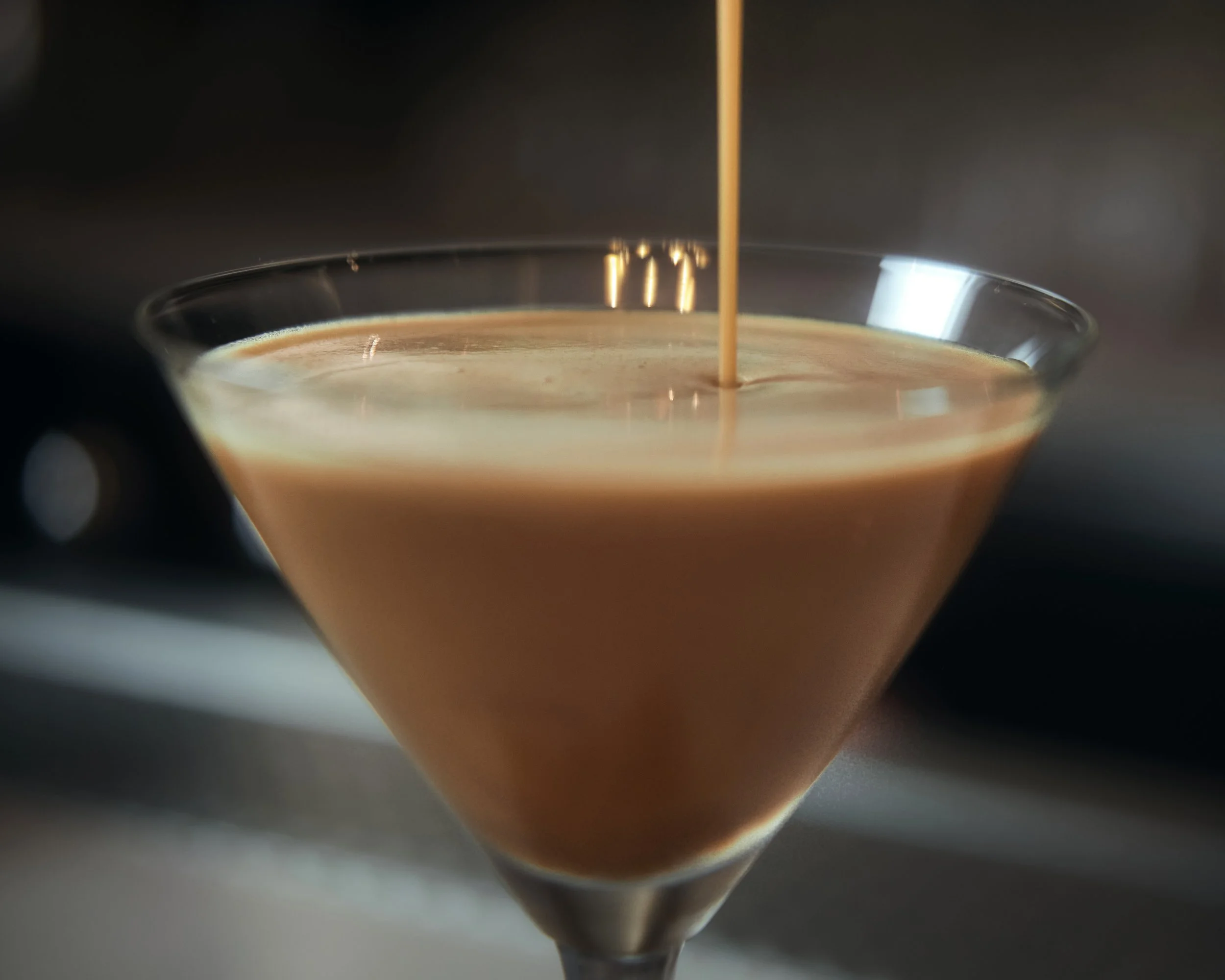 Hot espresso being poured into a clear glass cup.