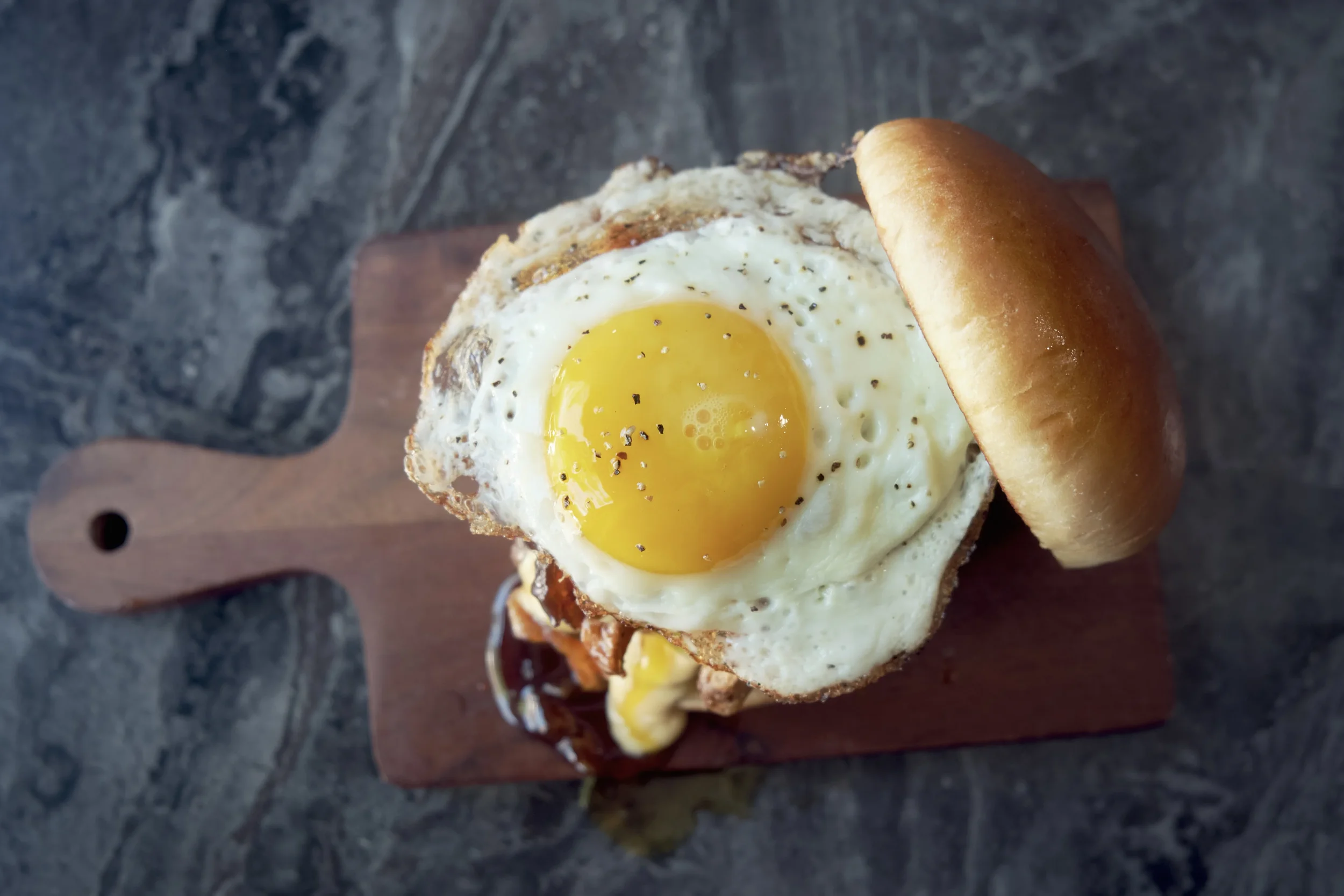 A sandwich with a fried egg on top, served on a wooden cutting board.