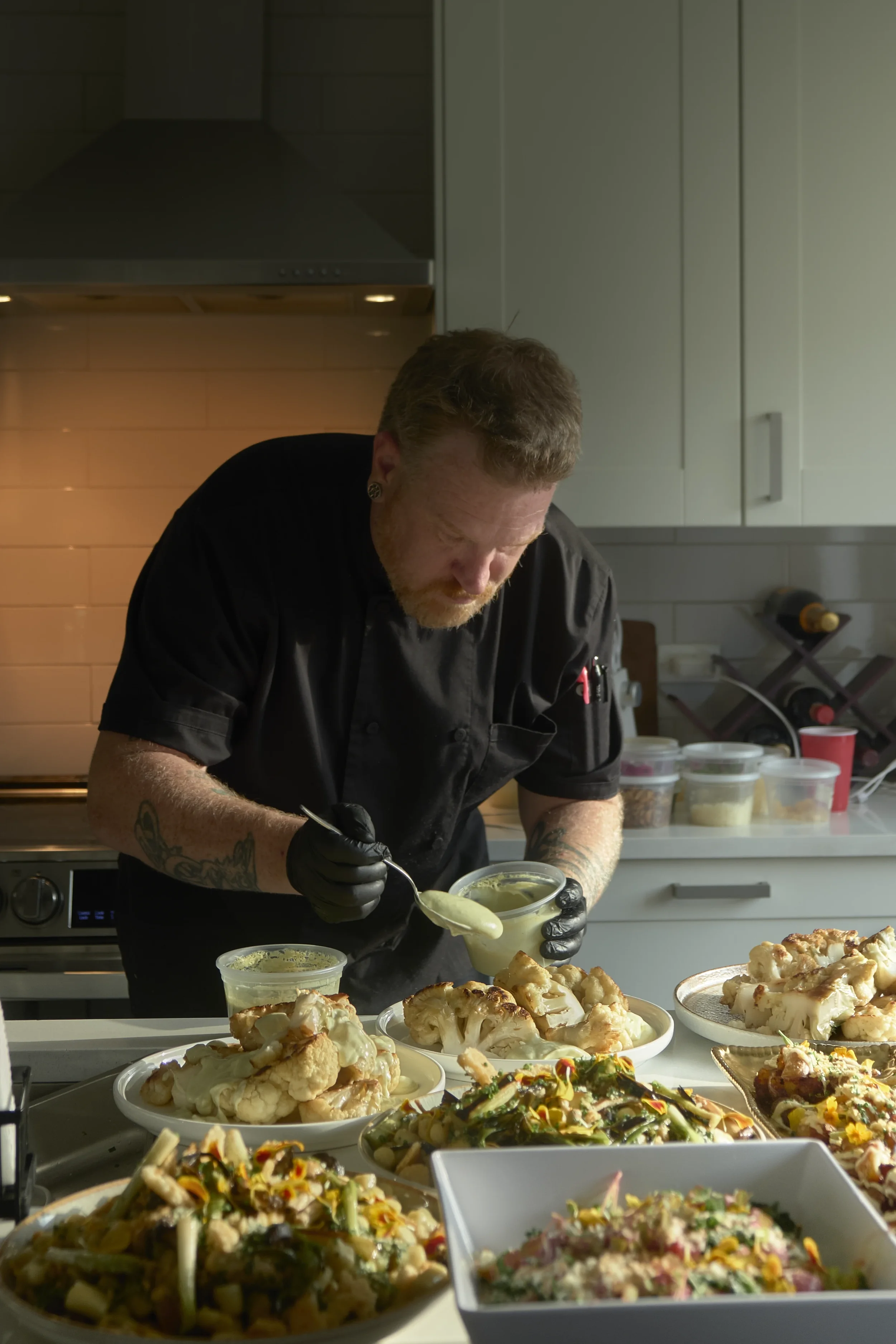 A chef in a black uniform preparing food in a professional kitchen, with various dishes and bowls of food on a counter in front.