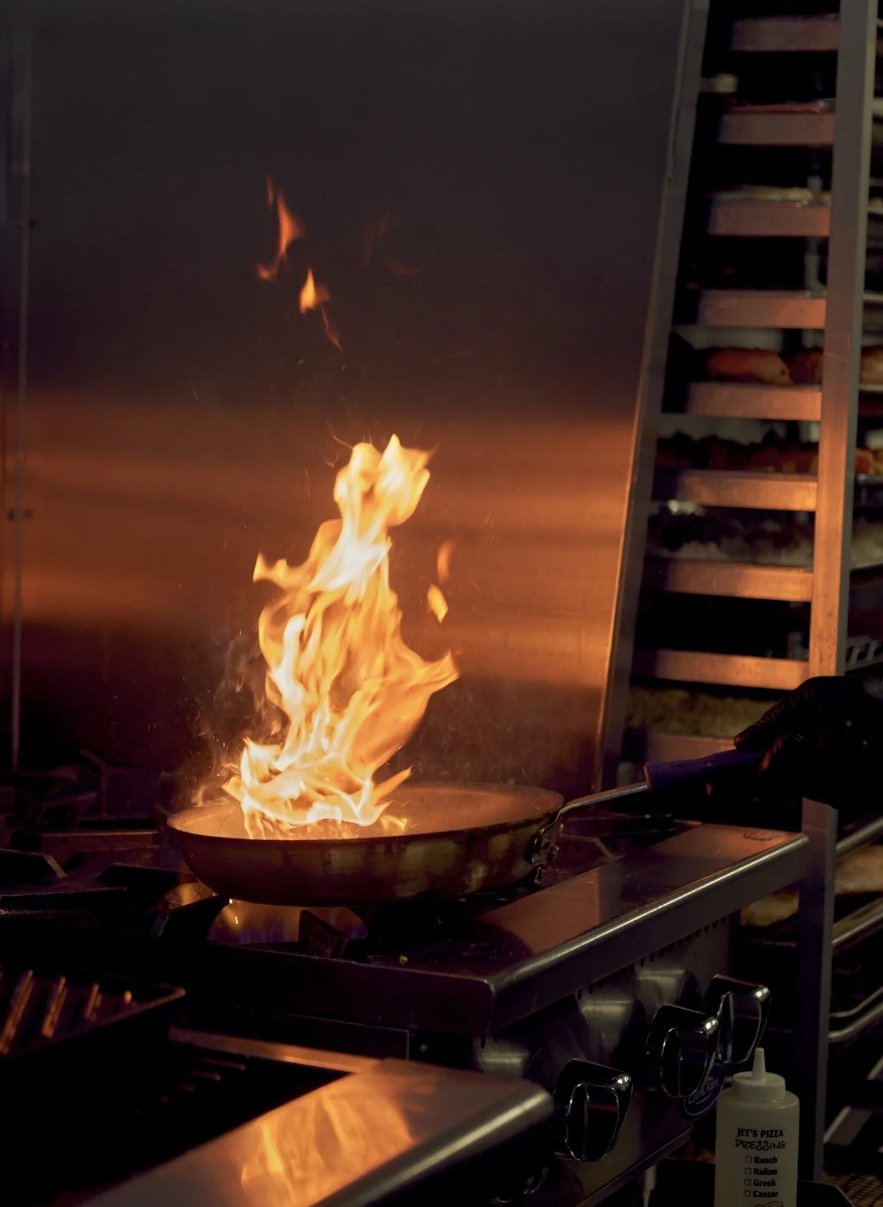 Flames in a frying pan on a stove in a restaurant kitchen.