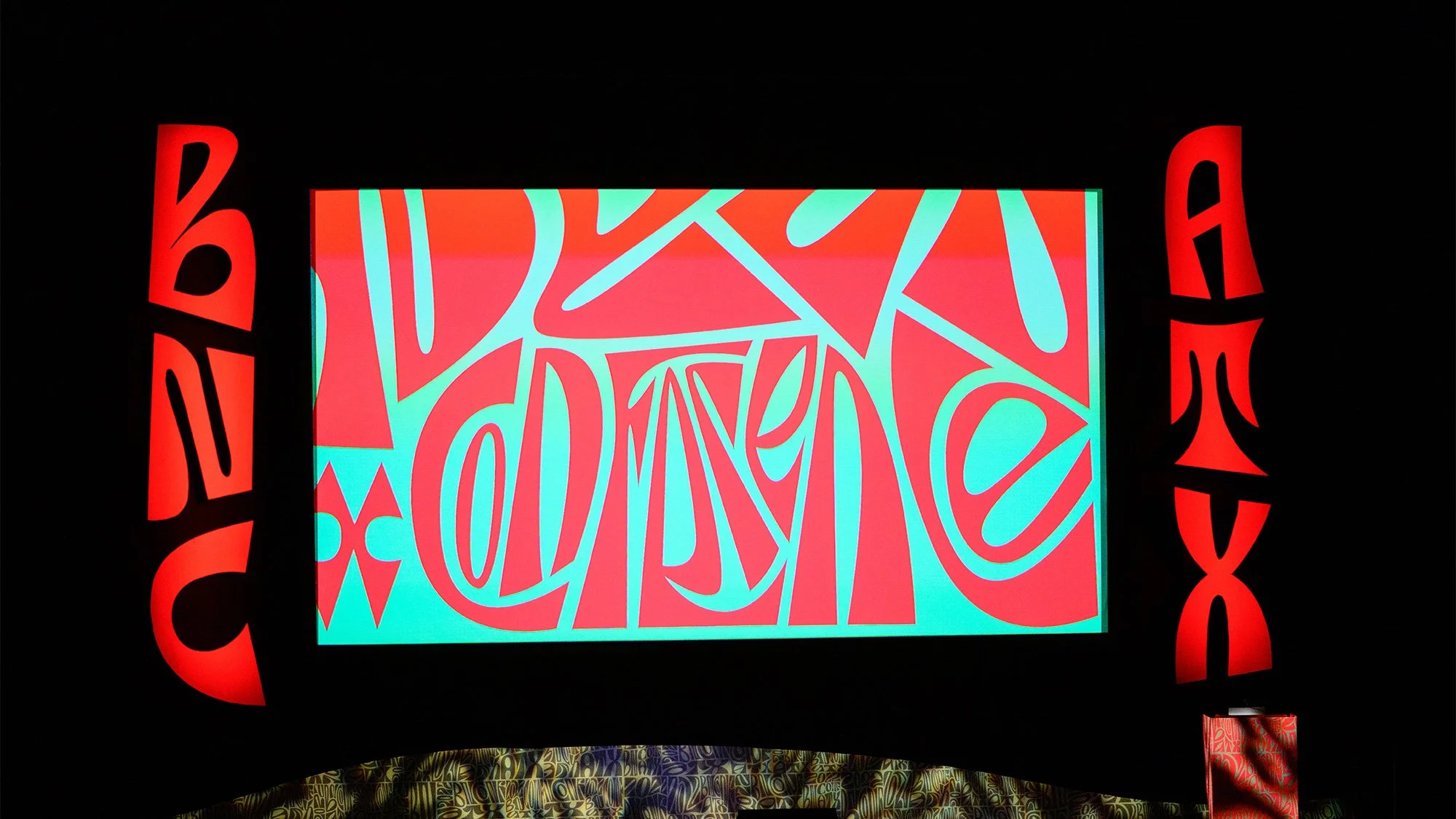 Colorful abstract art piece with blue, red, and pink shapes on a rectangular screen, surrounded by red curved text on a black background.
