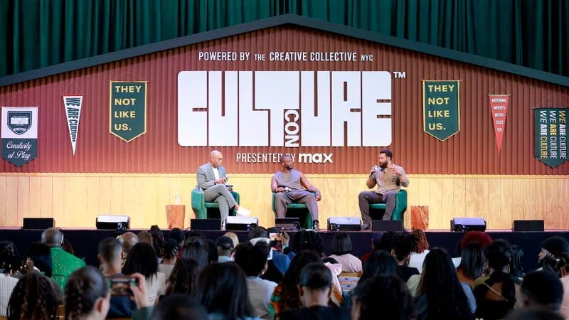 Panel discussion at the CultureCon conference with three speakers on stage, large banner behind them displaying 'CultureCon' and 'Powered by the Creative Collective NYC', audience facing the stage.