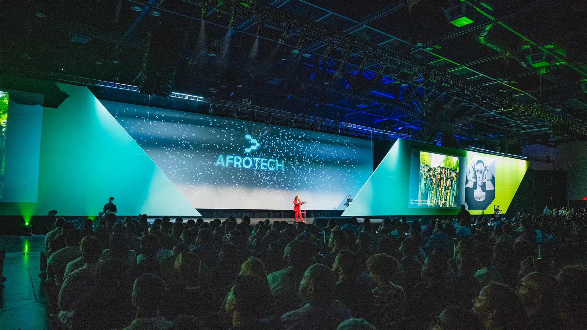 Large conference with a stage showing the words 'AFROTECH' on a big digital screen, audience seated in front, and presenters on stage.