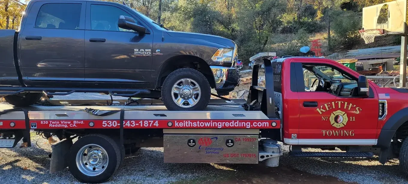 A red towing truck carrying a black Ram 2500 pickup truck.