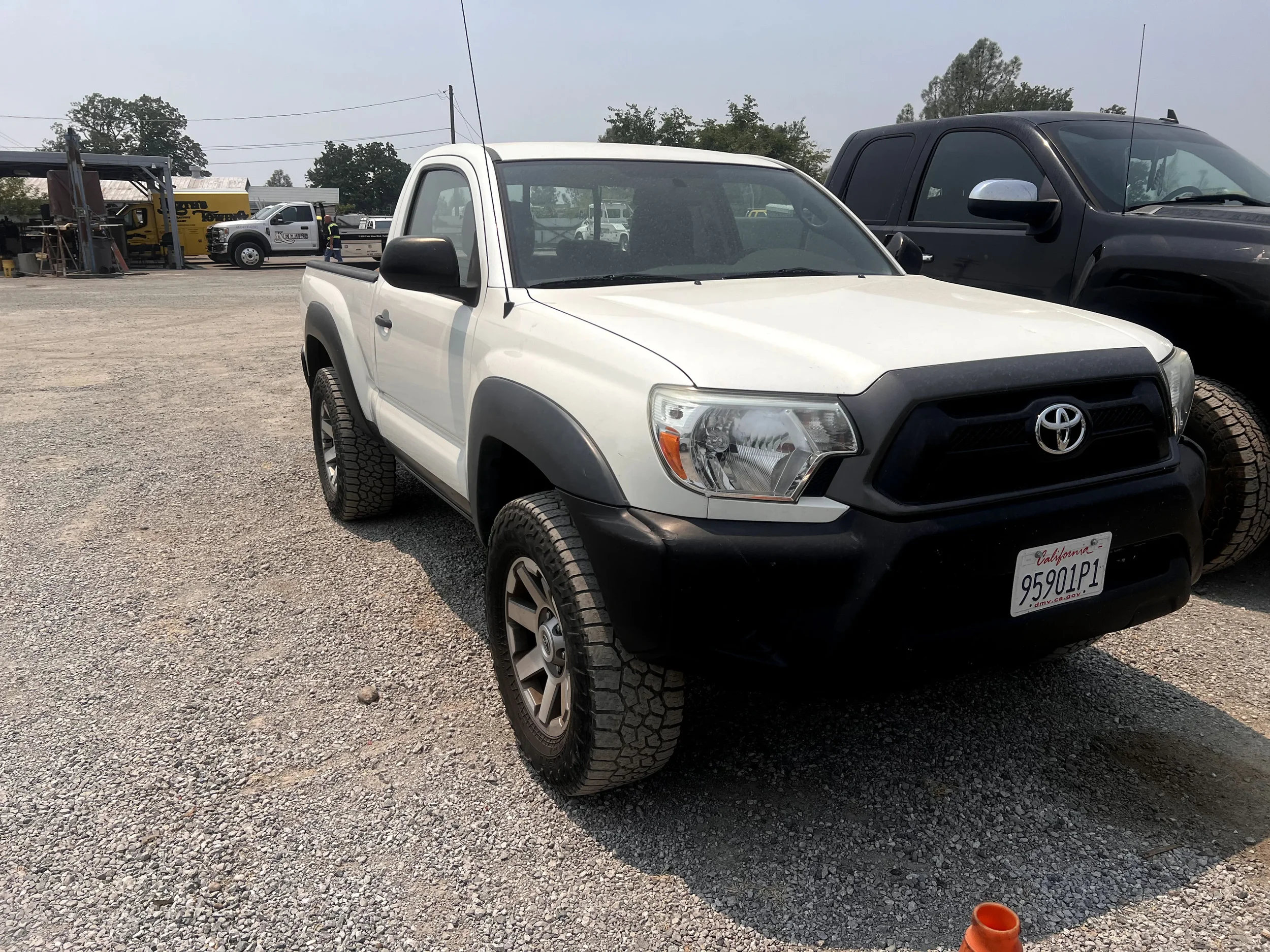 White Toyota Tacoma pickup truck with black front bumper and gray wheel arches parked on gravel lot.