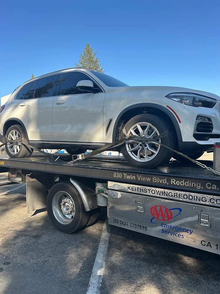 A white SUV is loaded on a flatbed tow truck in a parking lot with a clear blue sky above.