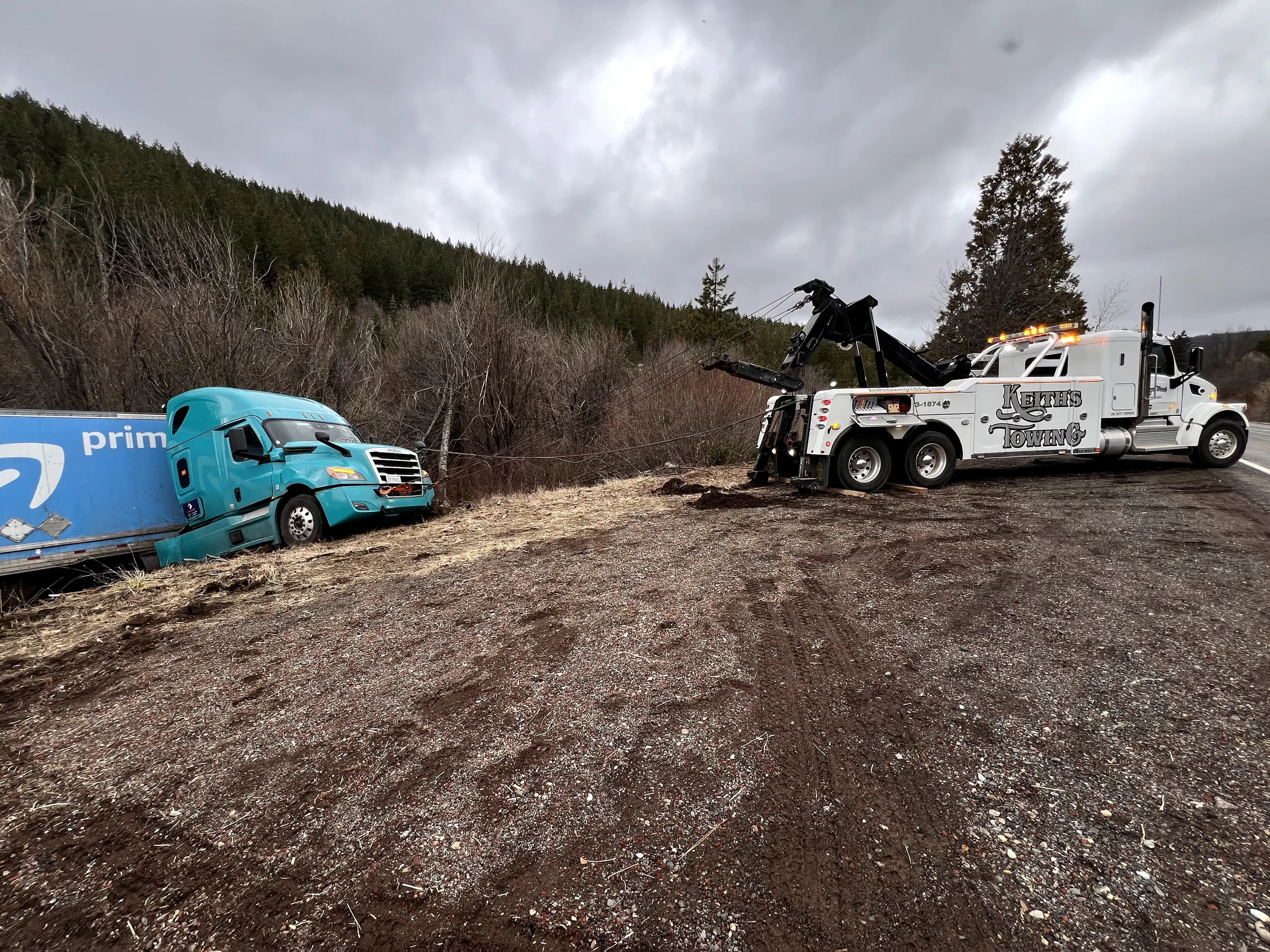 A truck has crashed into a ditch on the side of a rural road, with a tow truck on the scene.