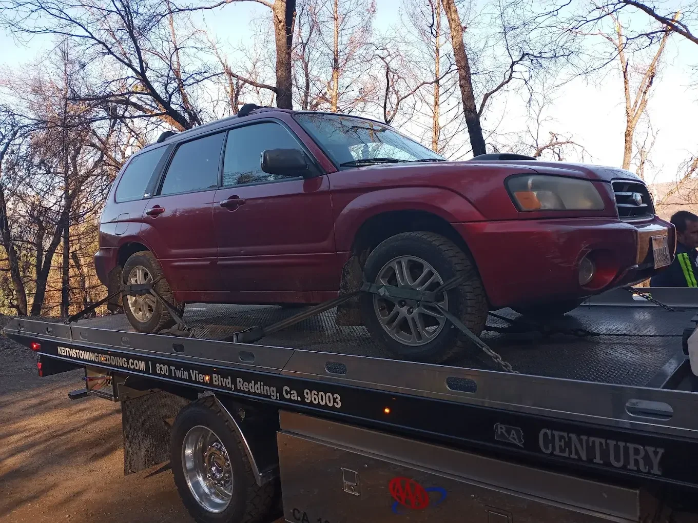 Red SUV secured on a flatbed tow truck with trees in the background.