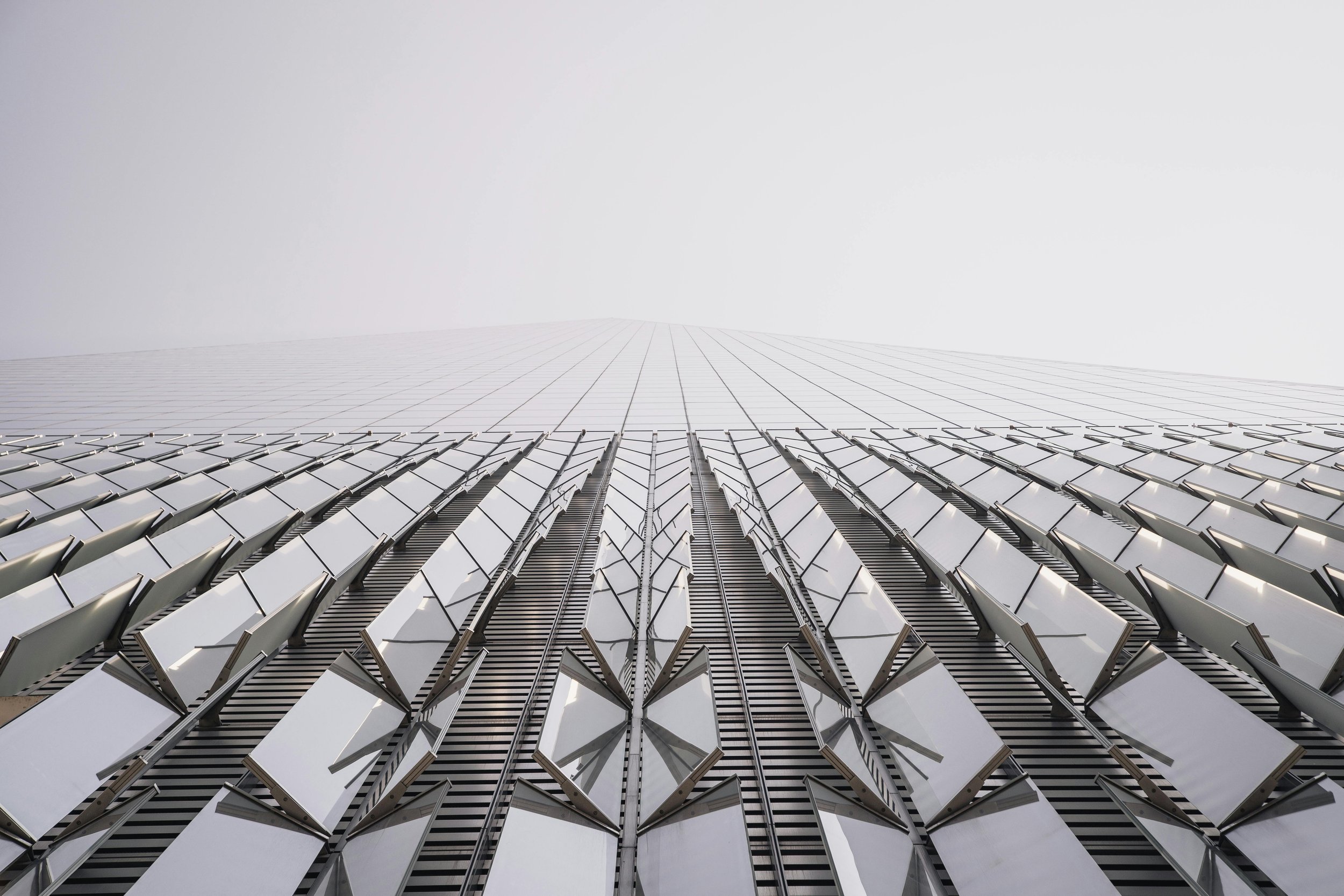 Low-angle view of a modern skyscraper with reflective glass windows and geometric architectural design fading into the foggy sky.