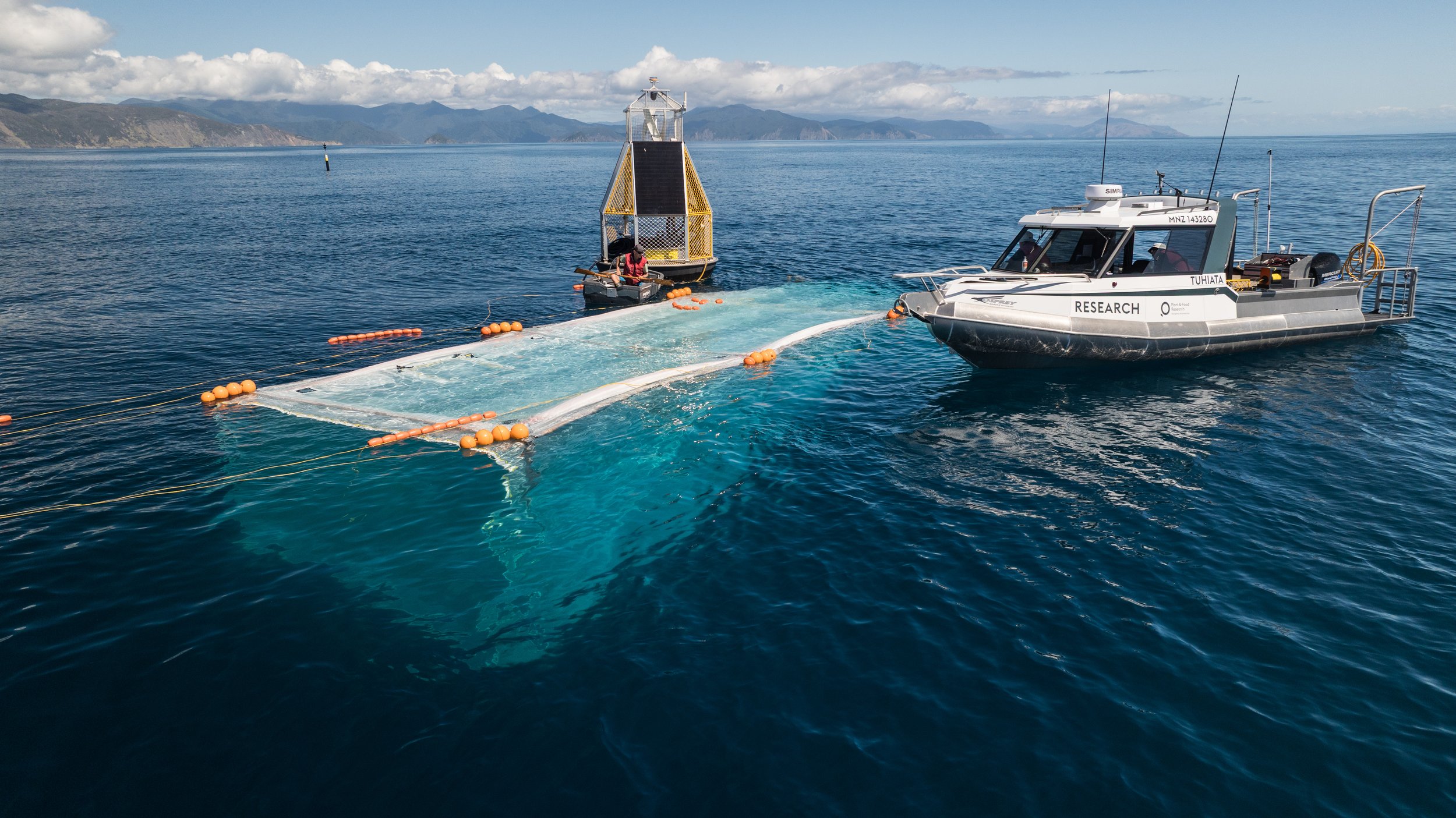 Research boat on the water retrieving a submerged object with a floating platform and underwater drone in a scenic ocean setting.