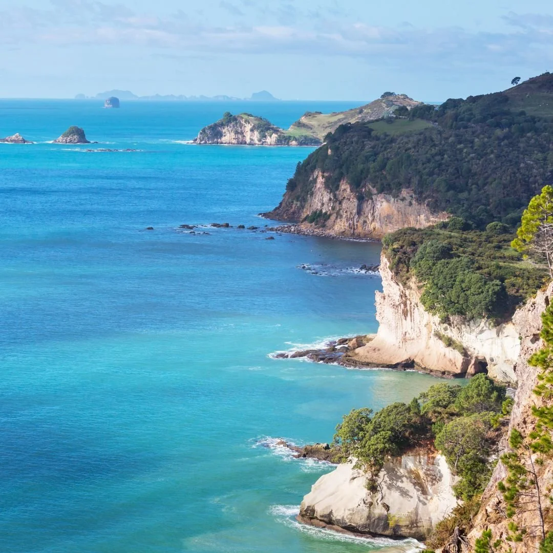 Scenic coastal landscape with turquoise water, rocky cliffs covered in greenery, and distant small islands.