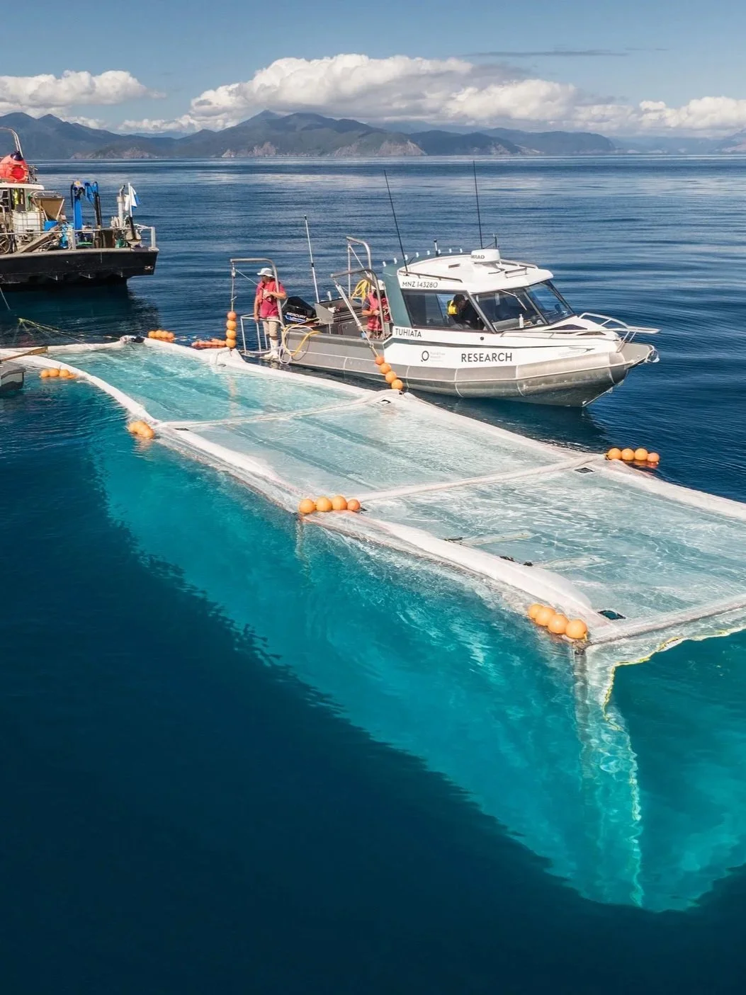 Research boat and aquatic equipment on a calm ocean with mountains in the background.
