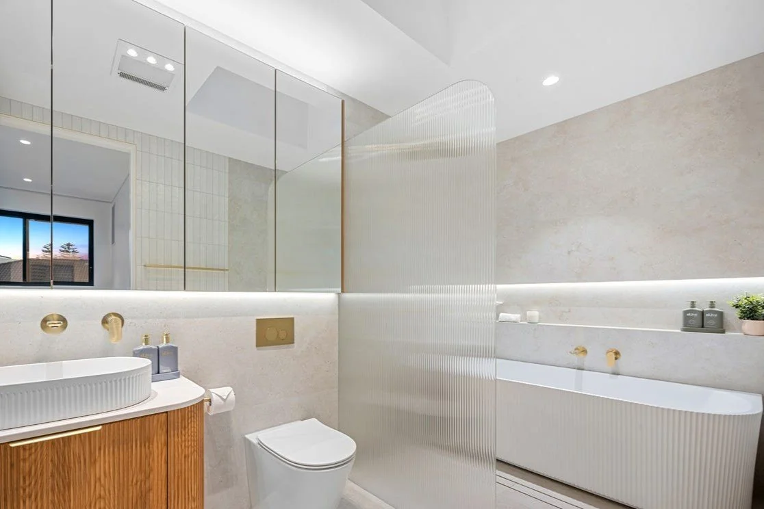 Modern bathroom with a white bathtub, a wooden vanity with an oval sink, and a mirrored wall.