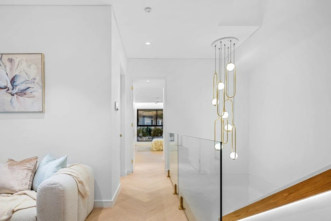 Modern interior hallway with white walls, light wood flooring, and a decorative hanging light fixture.