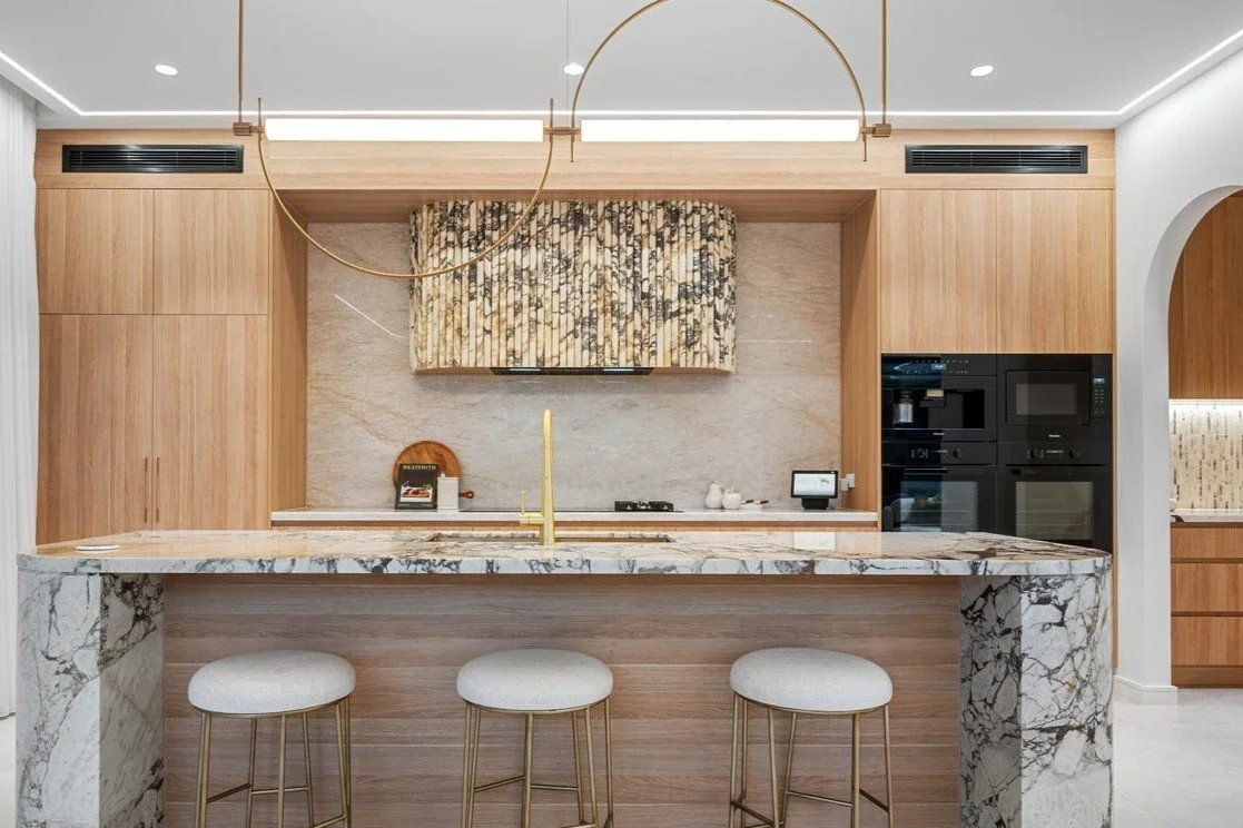 Modern kitchen with a marble island, wooden cabinetry, and a beige and black patterned window treatment.