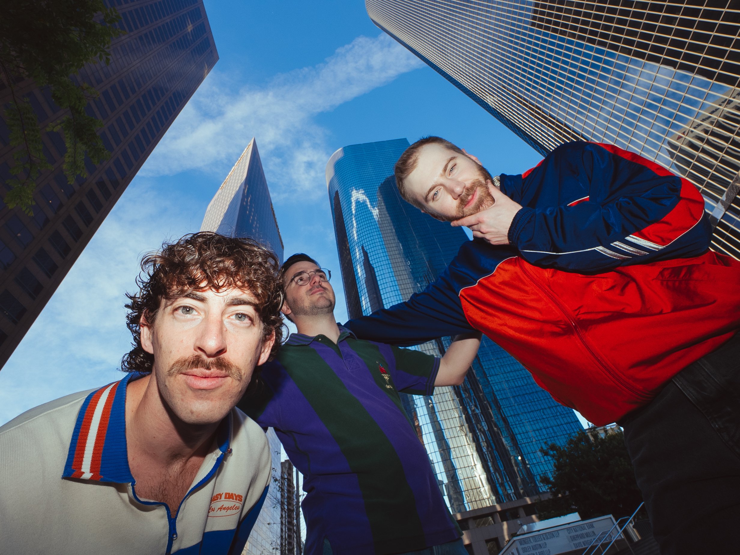Three men posing for a photo in a city with tall glass skyscrapers in the background
